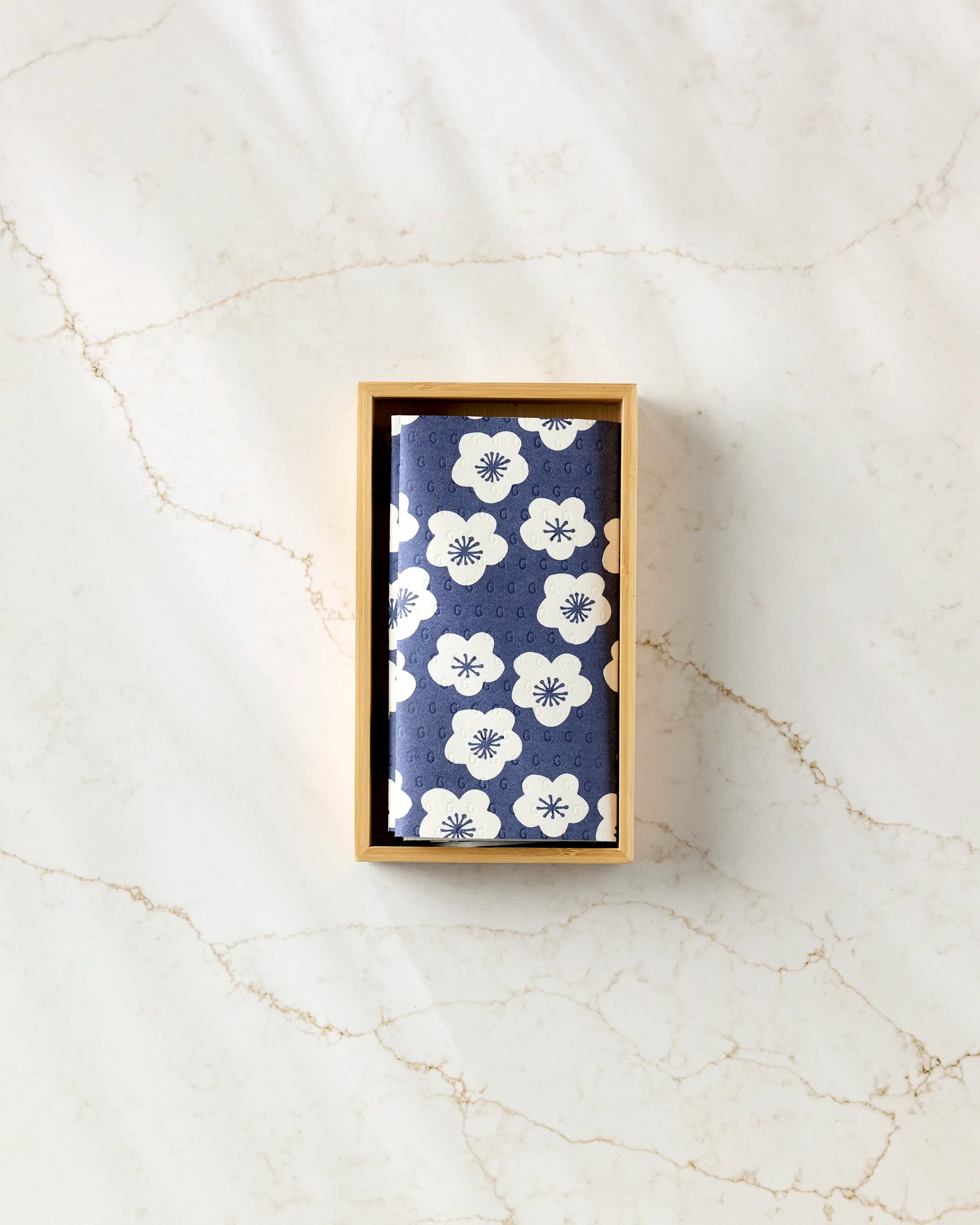 Every Wish by GEOMETRY features reusable paper towels with a navy blue and white floral pattern, artfully folded in a wooden box and elegantly displayed on a light, marbled surface.