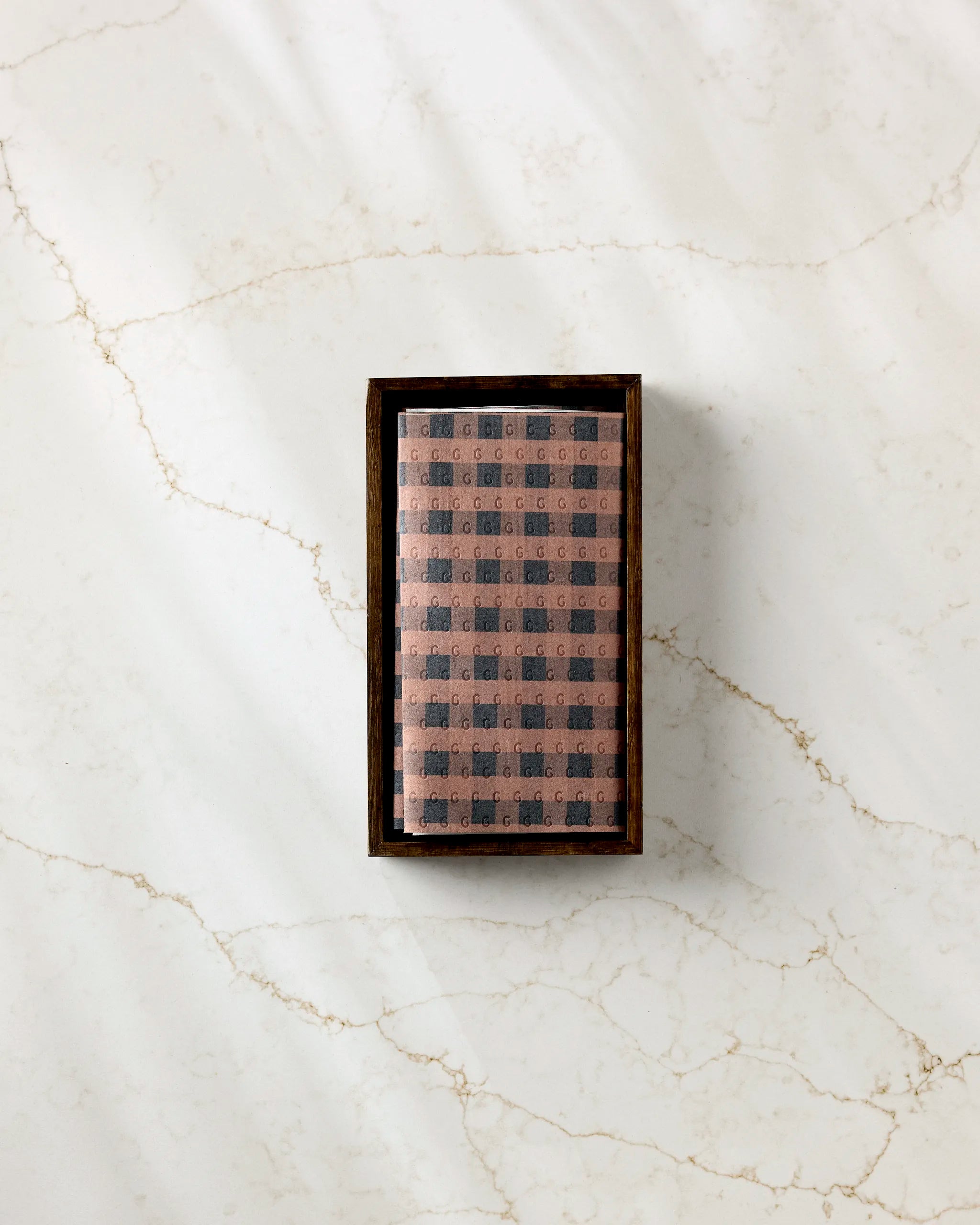 A rectangular Fall Gingham box by GEOMETRY, featuring a patterned two-tone design—ideal for storing eco-friendly kitchen towels—sits atop a white marble surface with light brown veins.