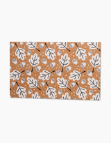 The Falling Acorns mat by Charlie Rowan Designs boasts a brown base with a repeating white oak leaf and acorn pattern outlined in black, plus scattered white circles—an eco-friendly substitute for paper towels.