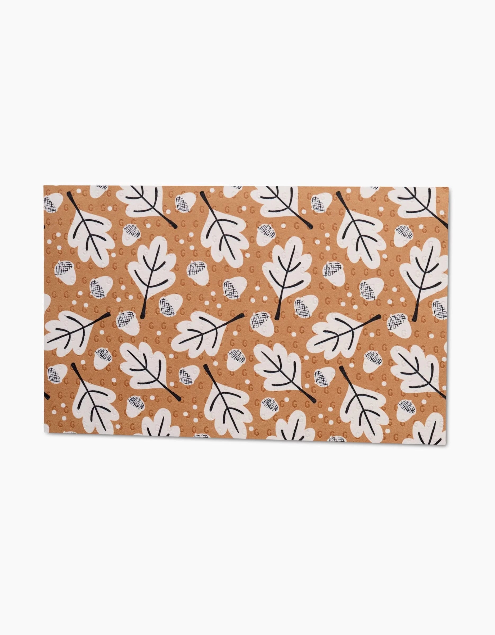 The Falling Acorns mat by Charlie Rowan Designs boasts a brown base with a repeating white oak leaf and acorn pattern outlined in black, plus scattered white circles—an eco-friendly substitute for paper towels.