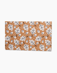 The Falling Acorns mat by Charlie Rowan Designs boasts a brown base with a repeating white oak leaf and acorn pattern outlined in black, plus scattered white circles—an eco-friendly substitute for paper towels.