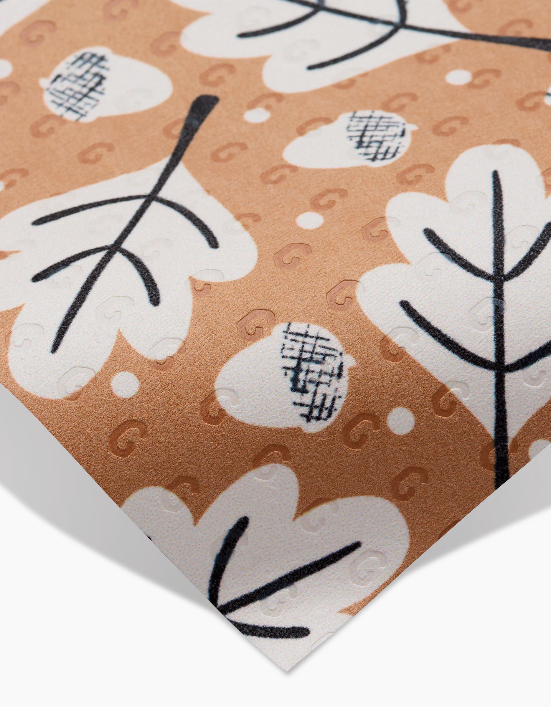A close-up of Falling Acorns by Charlie Rowan Designs: patterned, eco-friendly alternative paper featuring white leaves, black outlines, abstract crosshatch shapes, and tiny “G” letters—ideal as reusable paper towels on light brown.