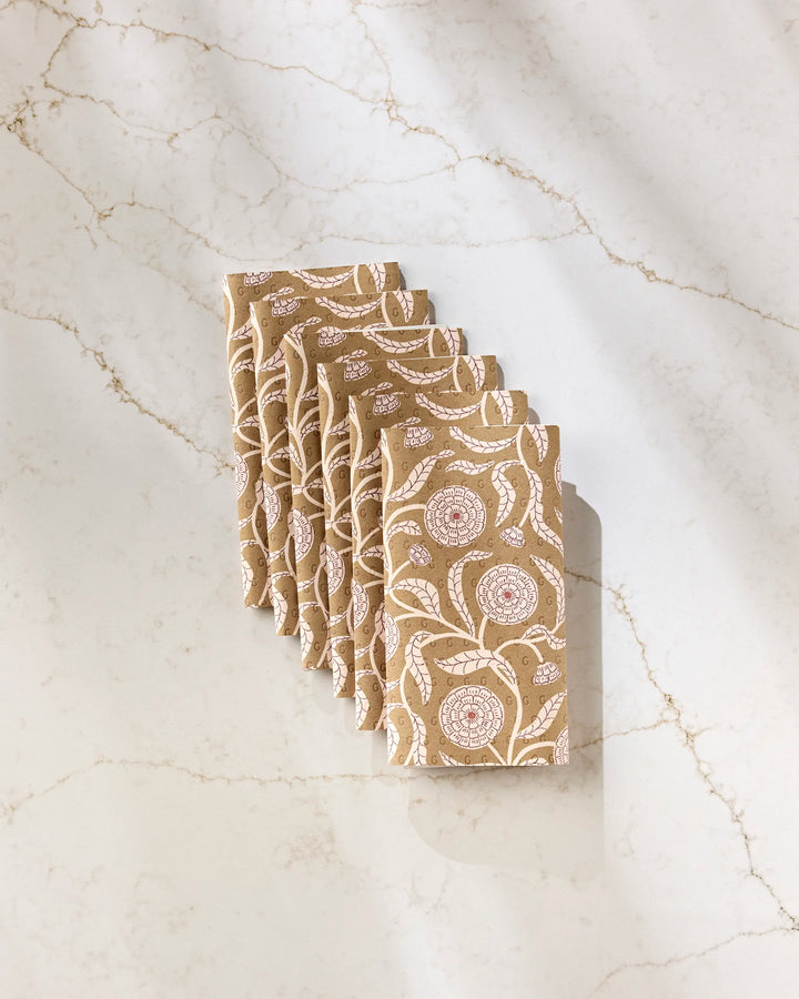 Six folded Falling Flowers reusable paper towels by Teri the Butter, featuring white and pink floral patterns, are neatly arranged in a row on a light marble surface with subtle veining.