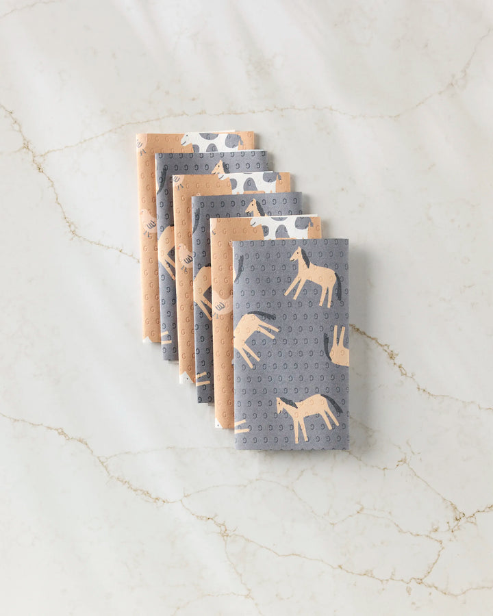 Six folded Farm Animals cloths by Coit Creative, arranged in a neat row on marble, feature grey and beige animal and dot patterns—an eco-friendly alternative to paper towels made from post-consumer recycled materials.