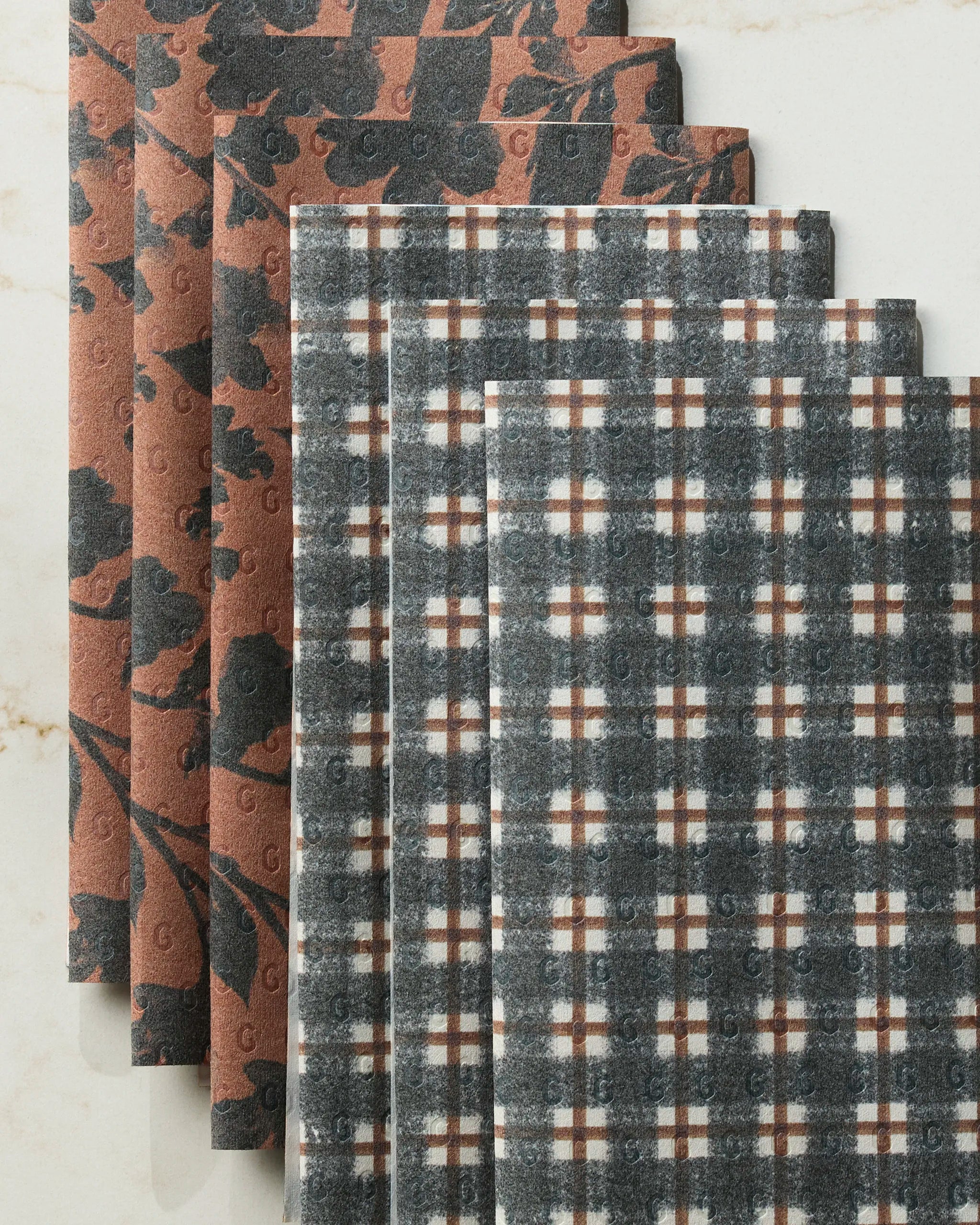 Two sets of Geometry Flint Hallowell reusable paper towels—one brown/black floral, one black/white/brown plaid—are displayed on a light marble surface.