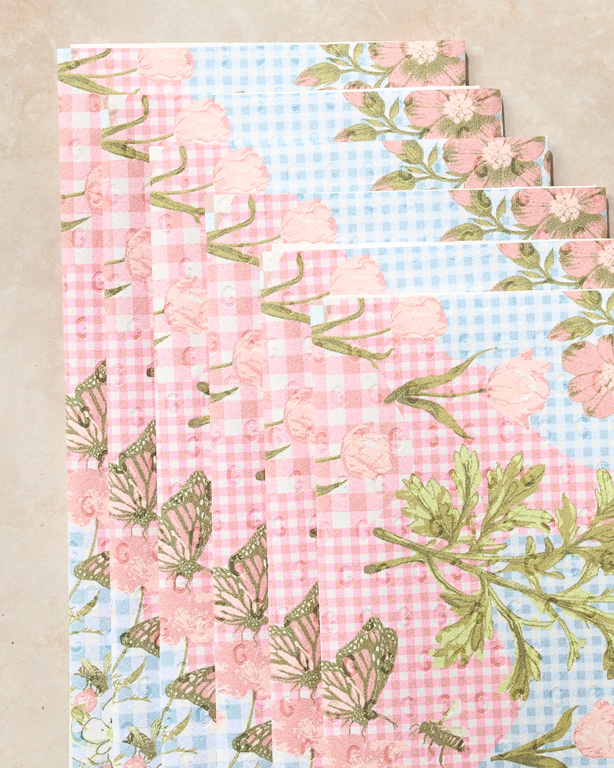 Five "Floral Collage" napkins by Geometry, featuring floral and butterfly prints with pink and blue checks, are fanned out on a light surface—ideal as eco-friendly paper towels for stylish, sustainable dining.
