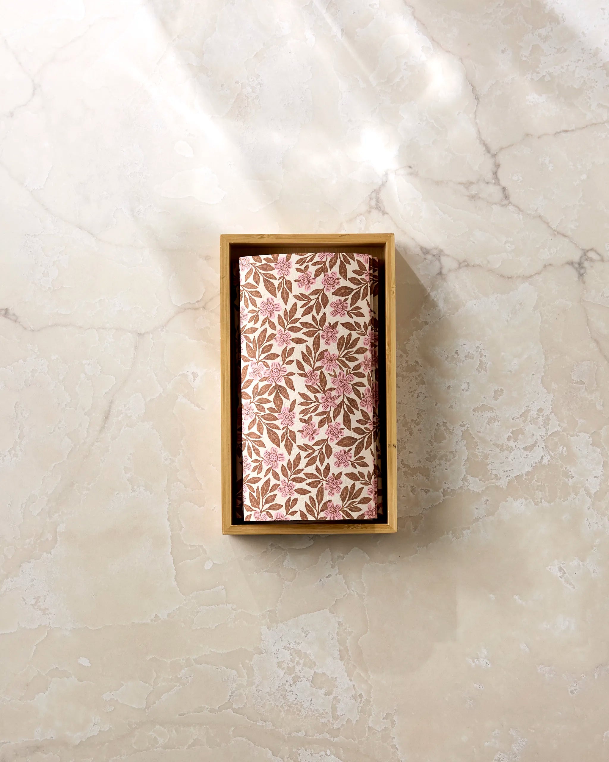 A Lisa Nelson "Floral Meadow" package, wrapped in eco-friendly paper towels with pink and brown leaves, sits in a rectangular wooden box on a light marble surface.