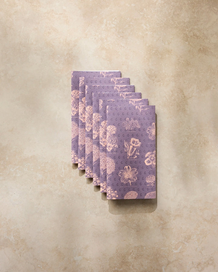 Seven Flower Glossary Orange notebooks by Geometry are neatly stacked on a beige, textured surface at an angle—evoking the organized look of reusable paper towels in an eco-friendly home.