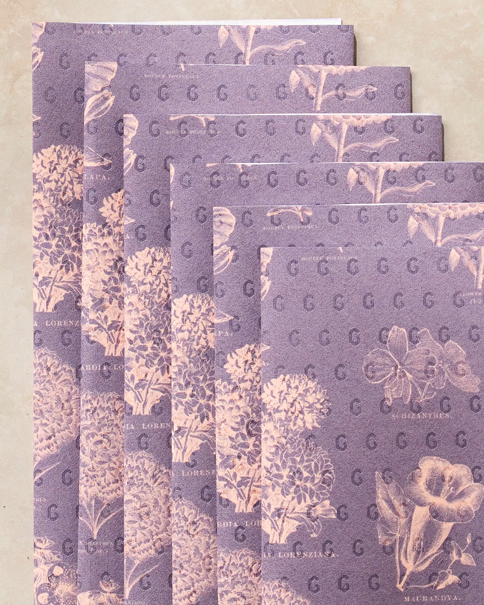 Six sheets of Flower Glossary Orange by Geometry, eco-friendly paper towels with a vintage botanical print in cream on orange, are displayed slightly fanned out on a light beige surface.