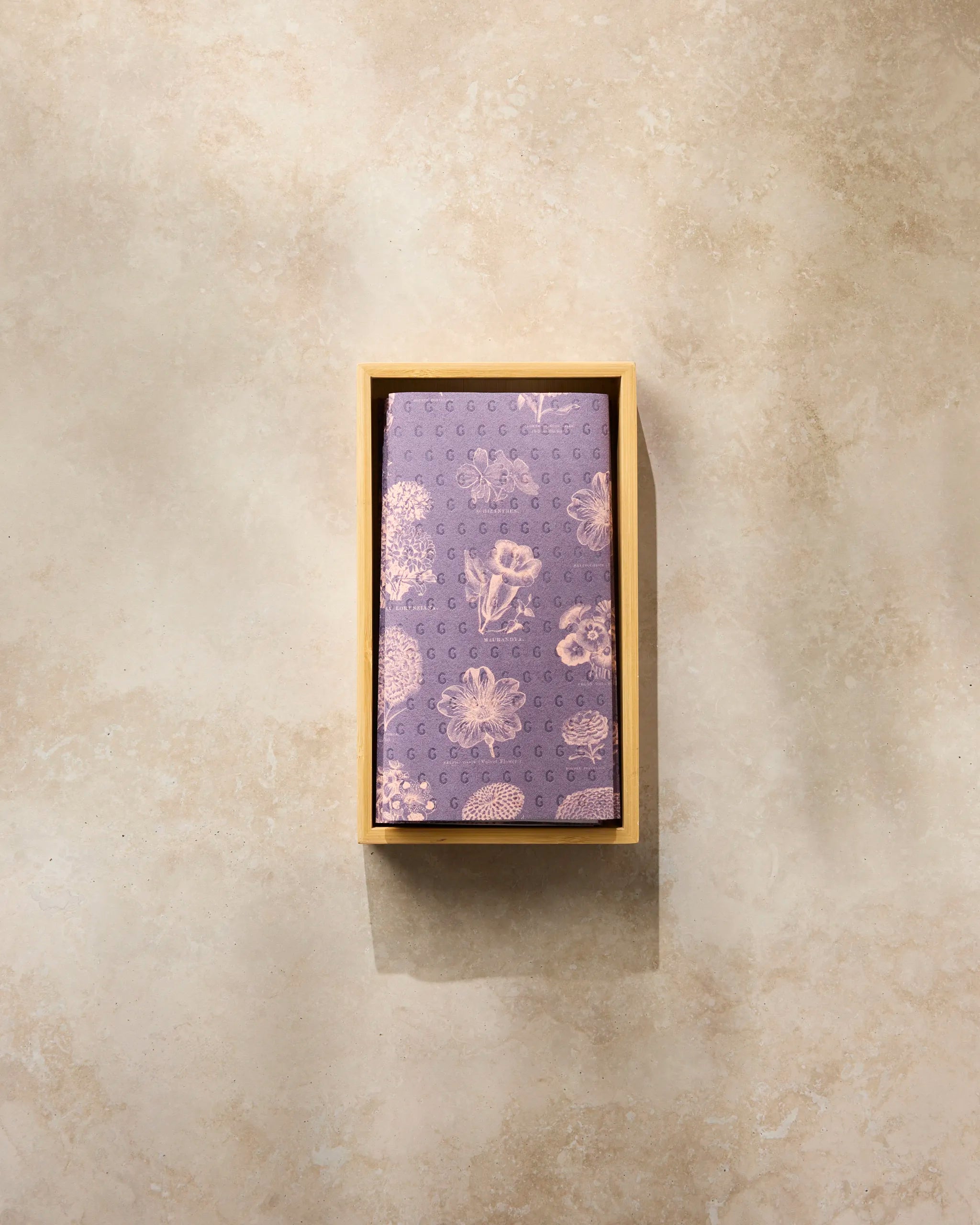 The Geometry Flower Glossary Orange kitchen towels are displayed beside a folded purple necktie with seashell and ocean patterns, both neatly arranged on a beige stone surface.