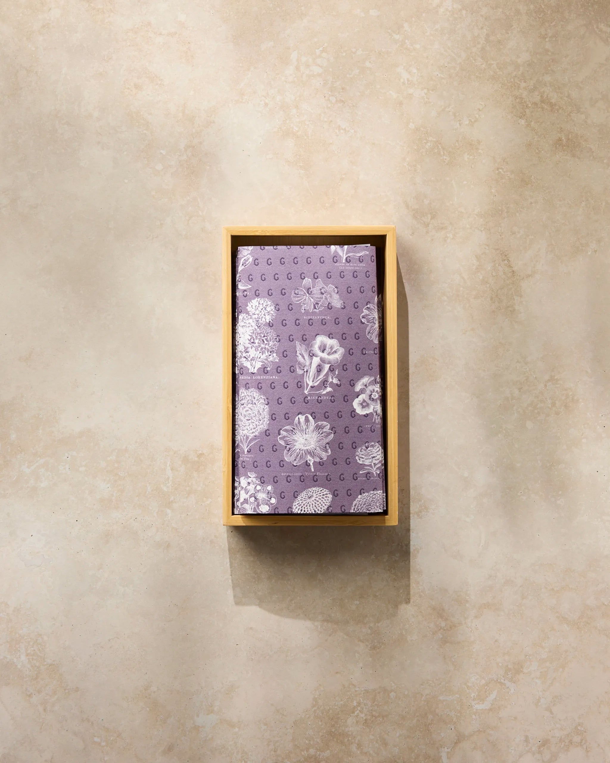 The Geometry Flower Glossary White handkerchief, neatly folded, rests in a rectangular wooden box on a light beige marble surface, showcasing its elegant white floral pattern.
