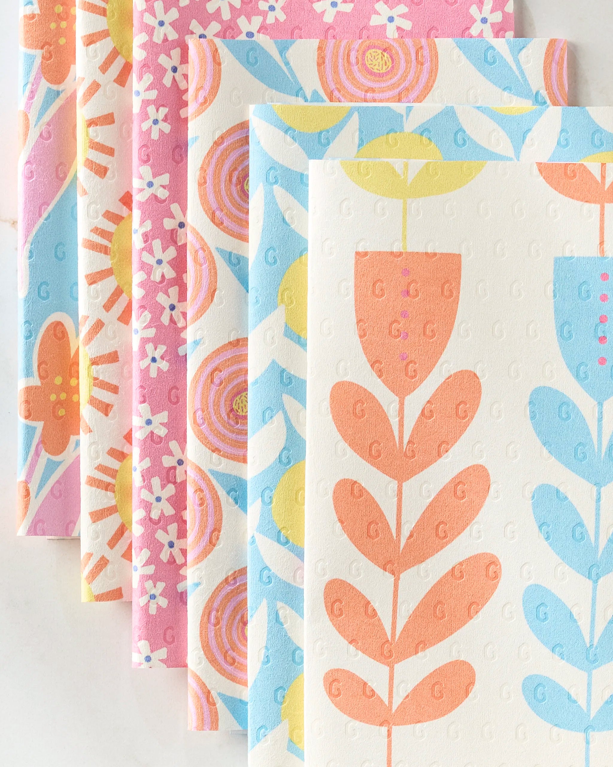 Lizzie Clark's Flower Parade features reusable paper towels with vibrant floral and geometric patterns in pink, orange, blue, and yellow, arranged neatly in an overlapping row on a white surface.