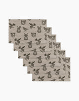 Six beige Forest Animals placemats by Rosa Kichline feature repeating cartoon faces of a bear, deer, and fox in dark brown. These eco-friendly kitchen towels are arranged in a slightly fanned-out stack.