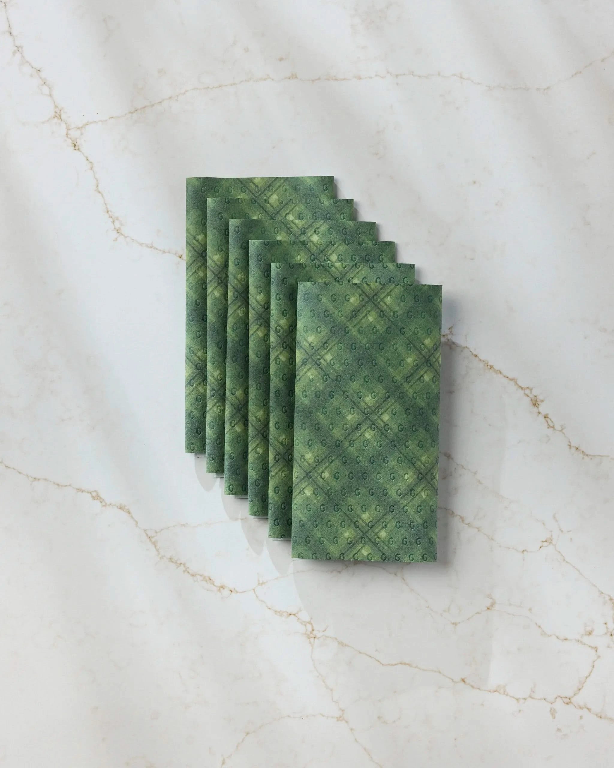 Seven Forever Plaid reusable paper towels by Geometry are fanned out diagonally on a white marble surface with subtle gold veining, casting soft shadows.