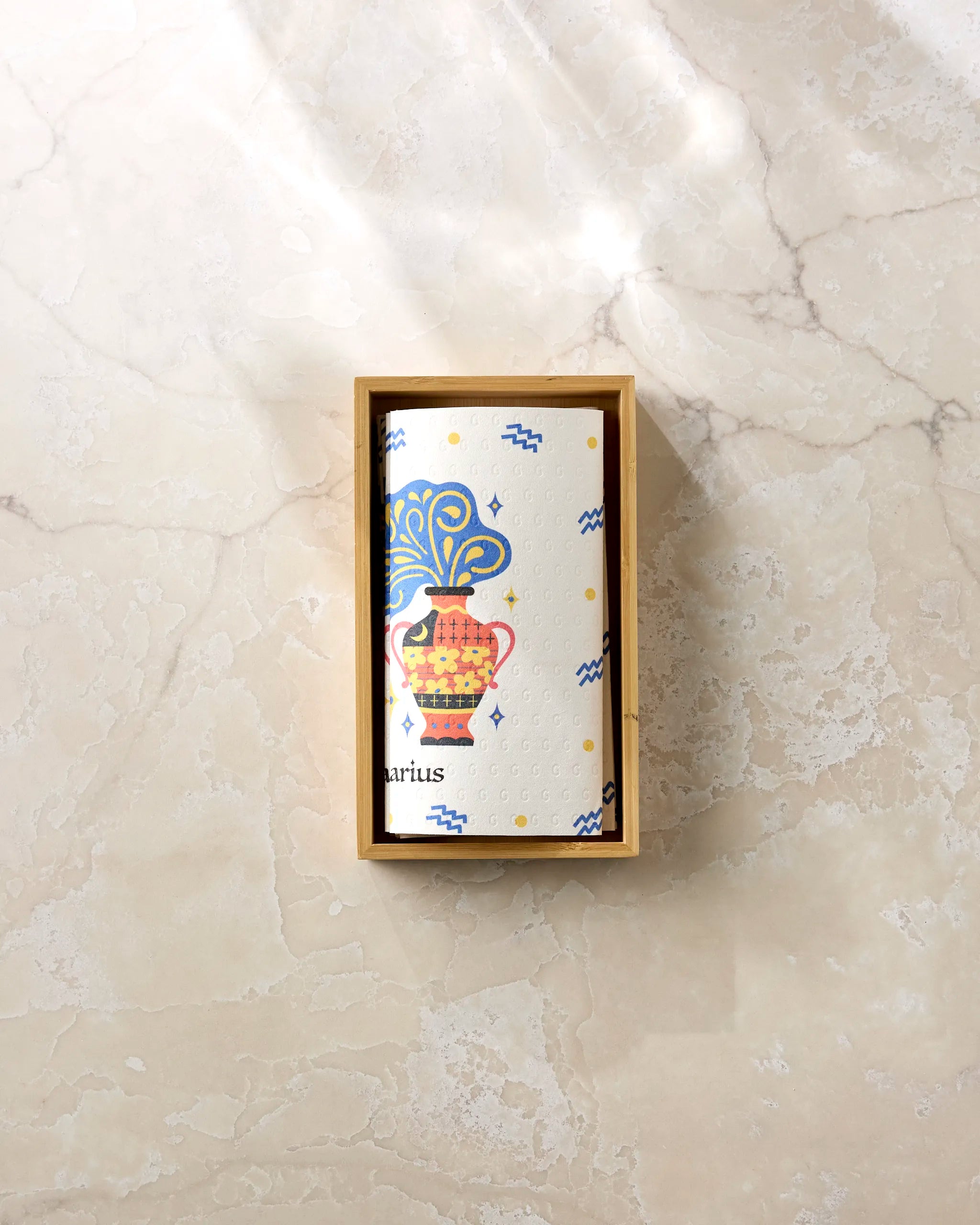 The Heather Zhou "Free Aquarius" roll features a vibrant Aquarius zodiac design with a decorated vase and blue waves, made from eco-friendly paper towels and displayed in a wooden box on a light marble surface.