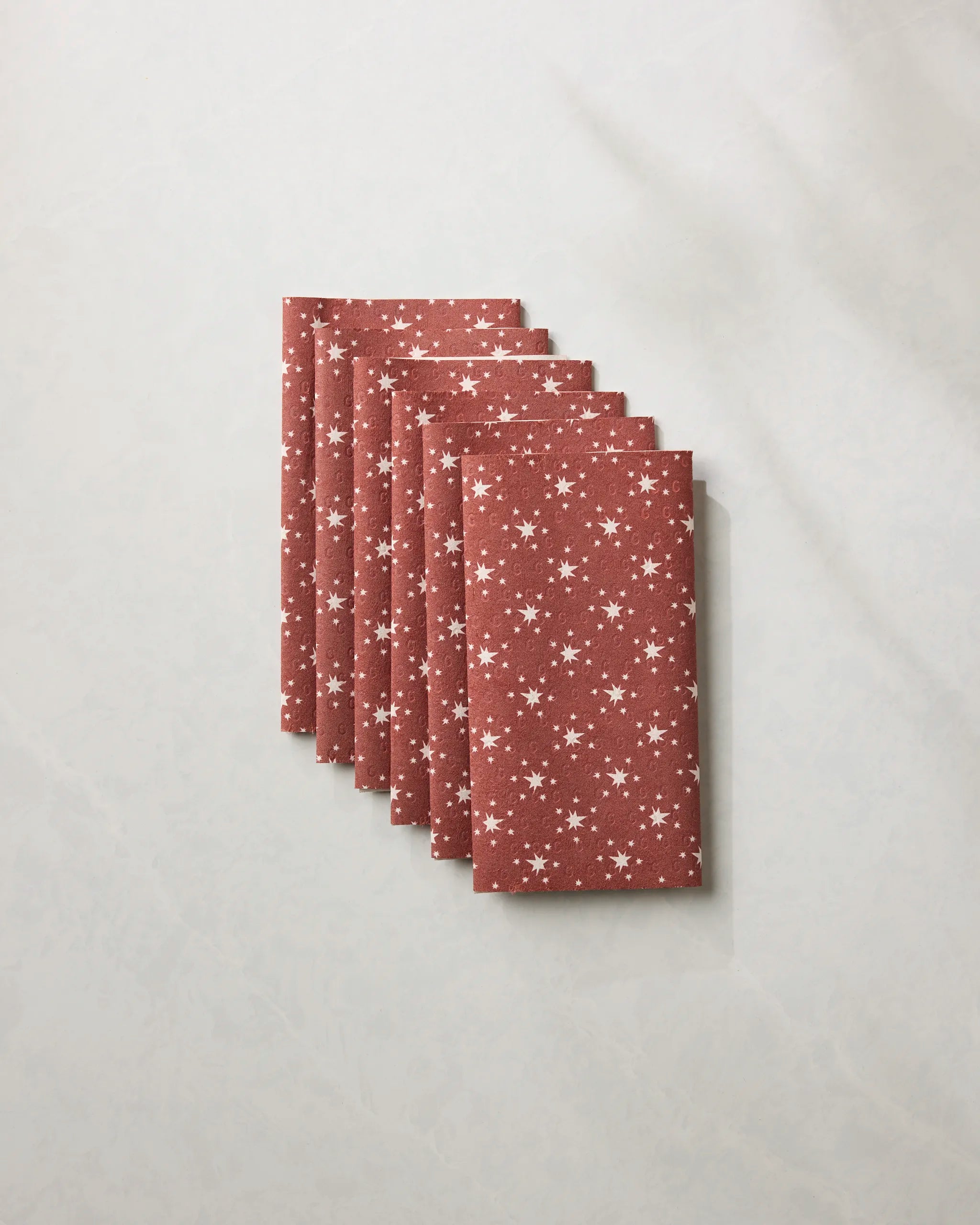 Six folded Freedom Red reusable paper towels by Geometry, featuring a rust color with white stars, are neatly fanned out on a light, textured surface.