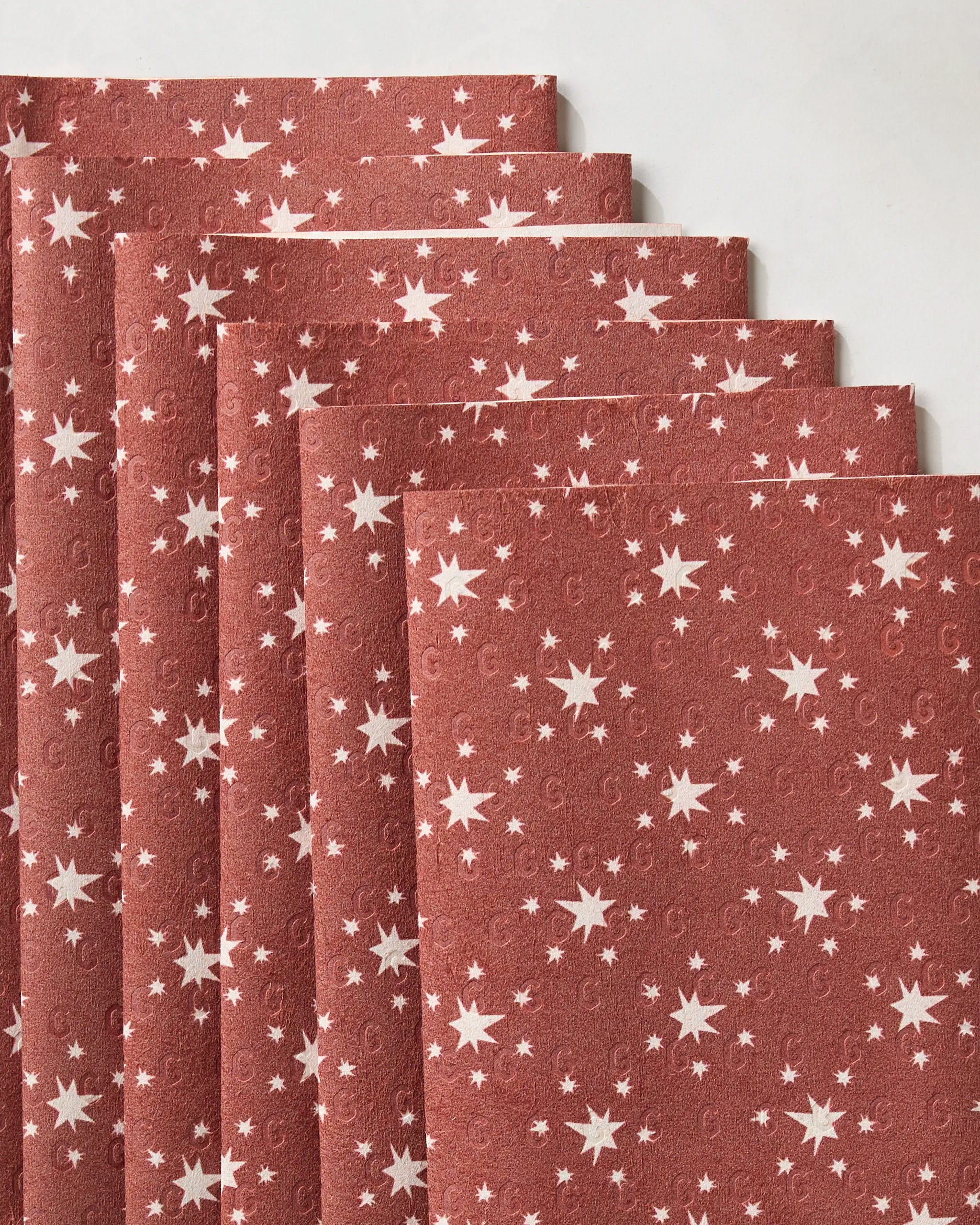 A neatly fanned stack of Geometry Freedom Red reusable paper towels, featuring a brownish-red color with white stars and small G letters, displayed against a light background.