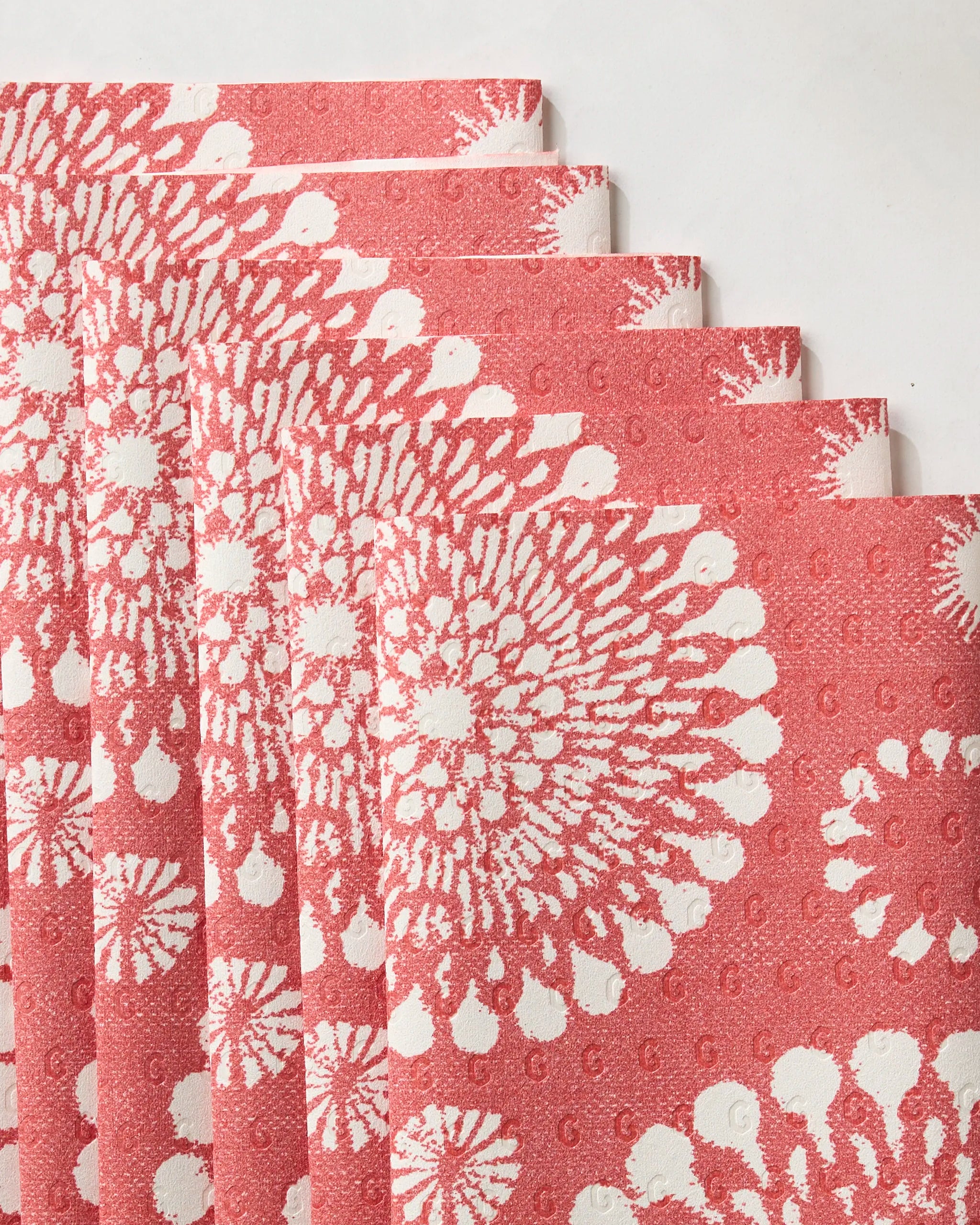 Six sheets of Geometry's Freedom Sparks Bright, eco-friendly textured red paper towels with white circular floral patterns are fanned out on a white background.