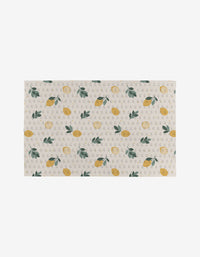 The Sara Mari Freshly Picked mat features a rectangular beige design with yellow lemons, green leaves, and gray Gs on a light background—crafted from recycled materials for an eco-friendly touch.