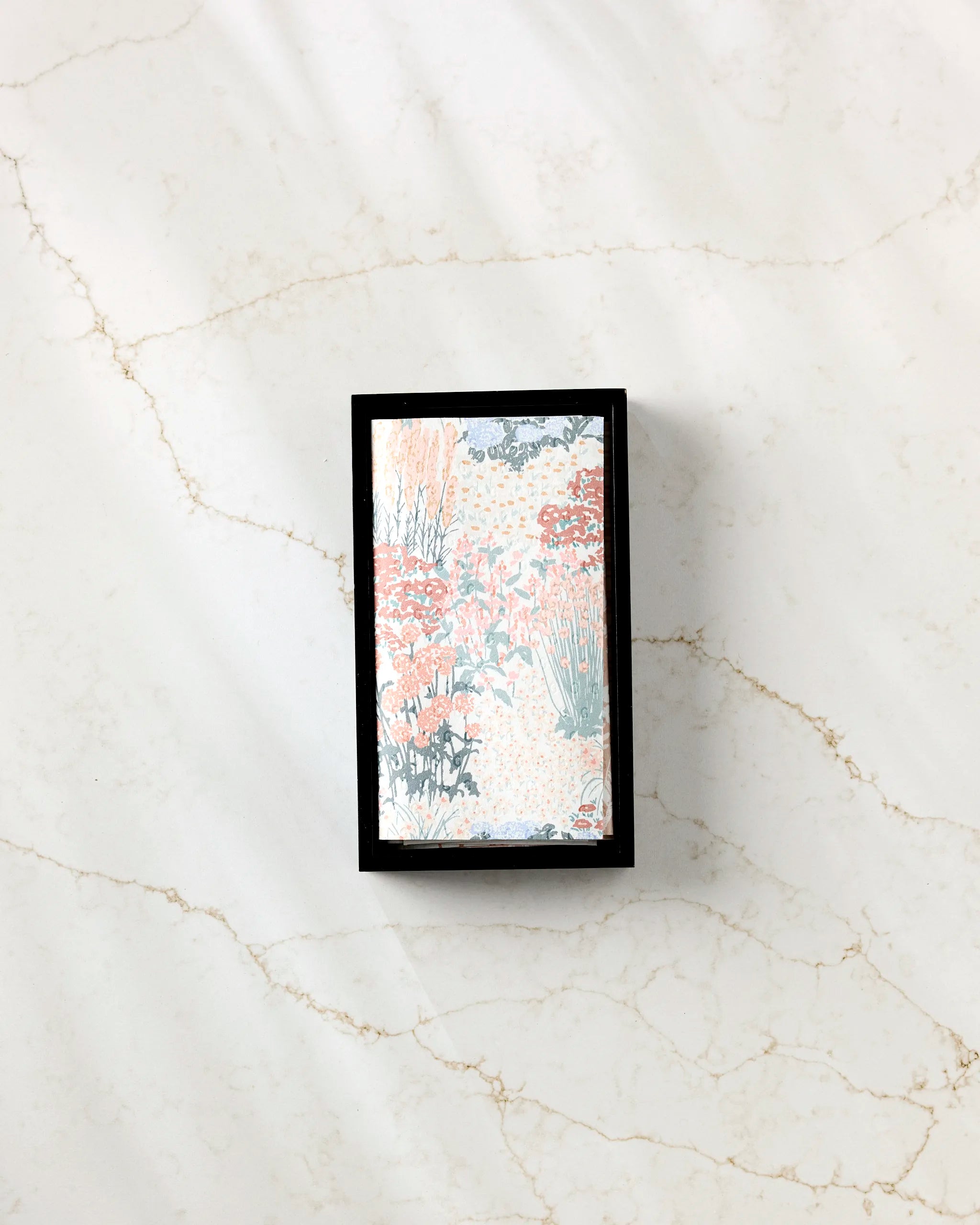 A Garden Bloom rectangular box of eco-friendly paper towels by Hufton Studio, featuring a pastel floral lid, sits on a white marble surface with light brown veining.