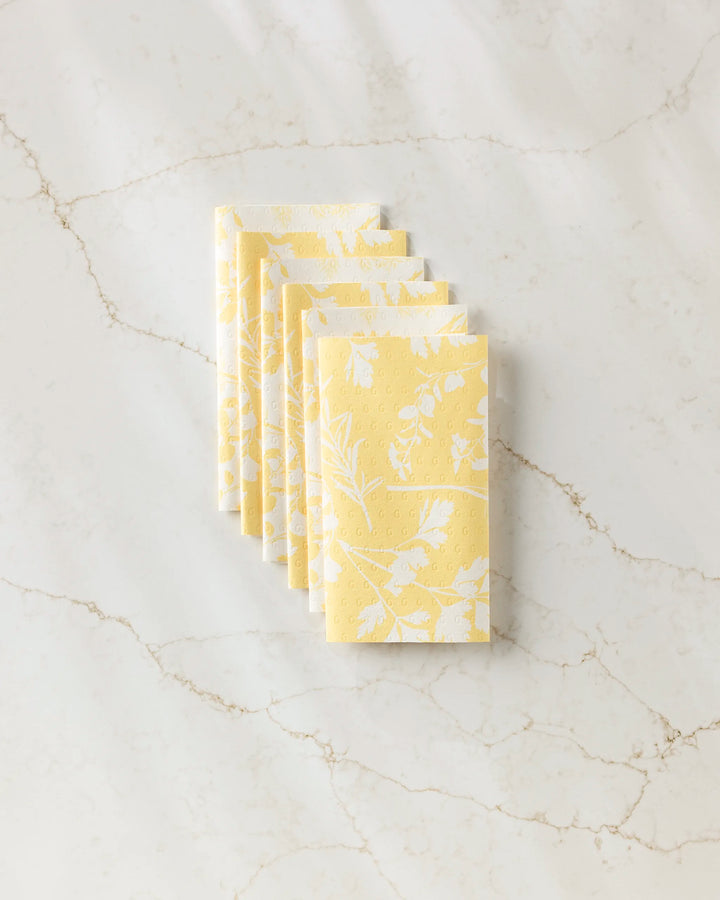 A stack of six folded GEOMETRY Garden of Gold yellow reusable paper towels with a white floral pattern, displayed on a white marble surface with subtle veining.