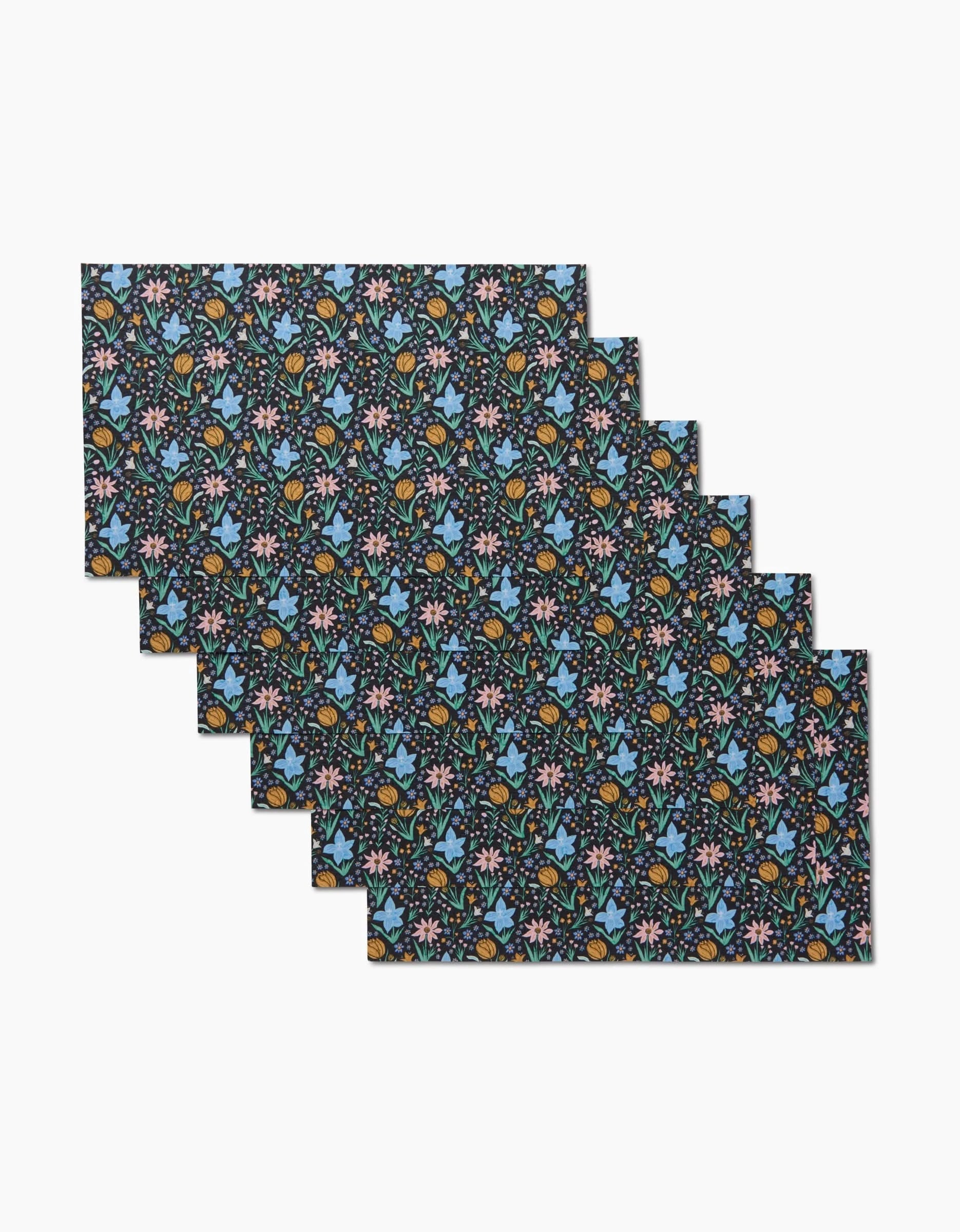 Six Garden of Light placemats by Danelys Sidron feature a vibrant floral pattern on a dark background. Made from eco-friendly materials, theyre perfect for creating a stylish, sustainable table setting.