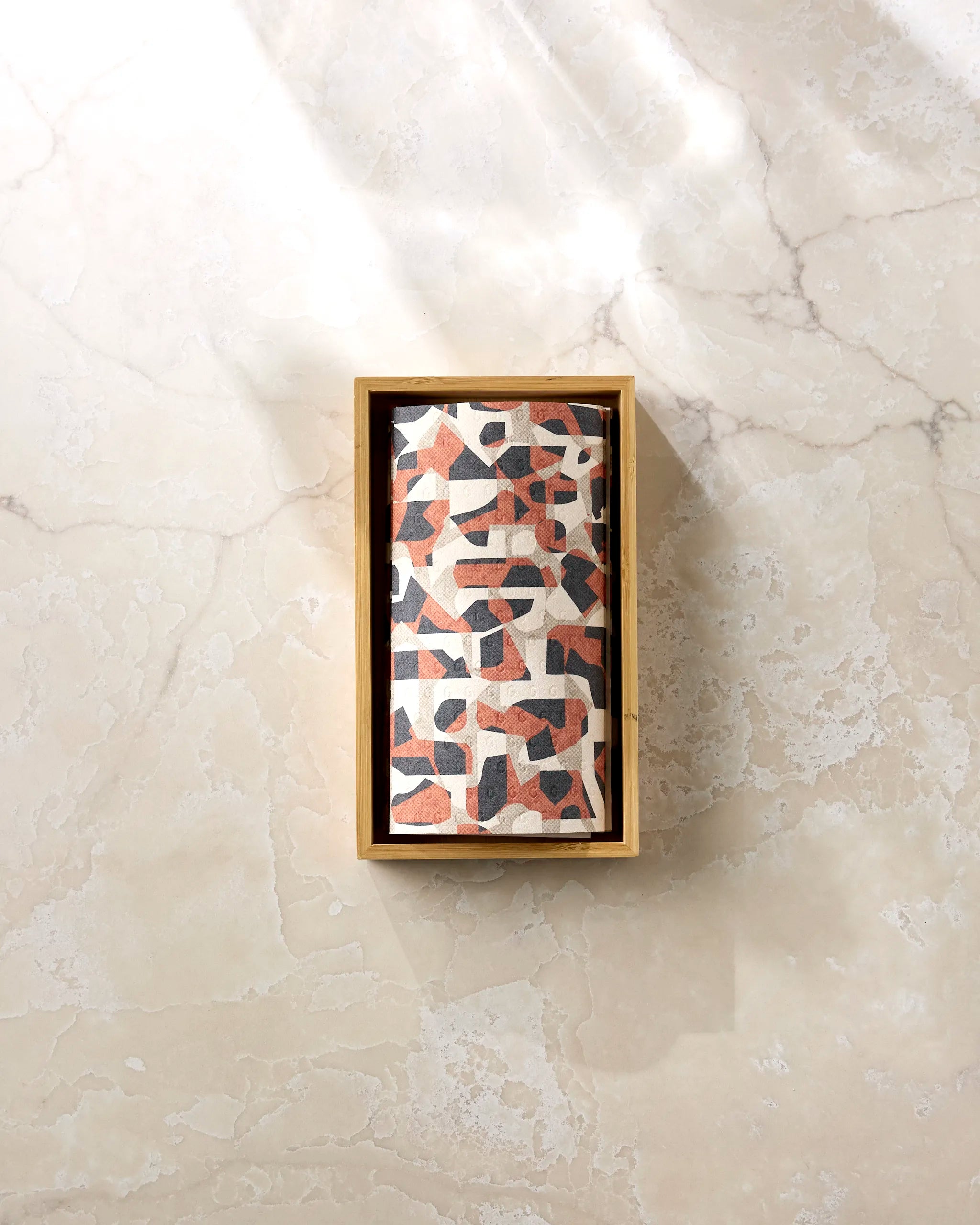 The Kris Ruff Geometric Leopard reusable paper towels come in a rectangular wooden box, wrapped in geometric-patterned paper with earthy tones and displayed on a light marble surface under soft sunlight.