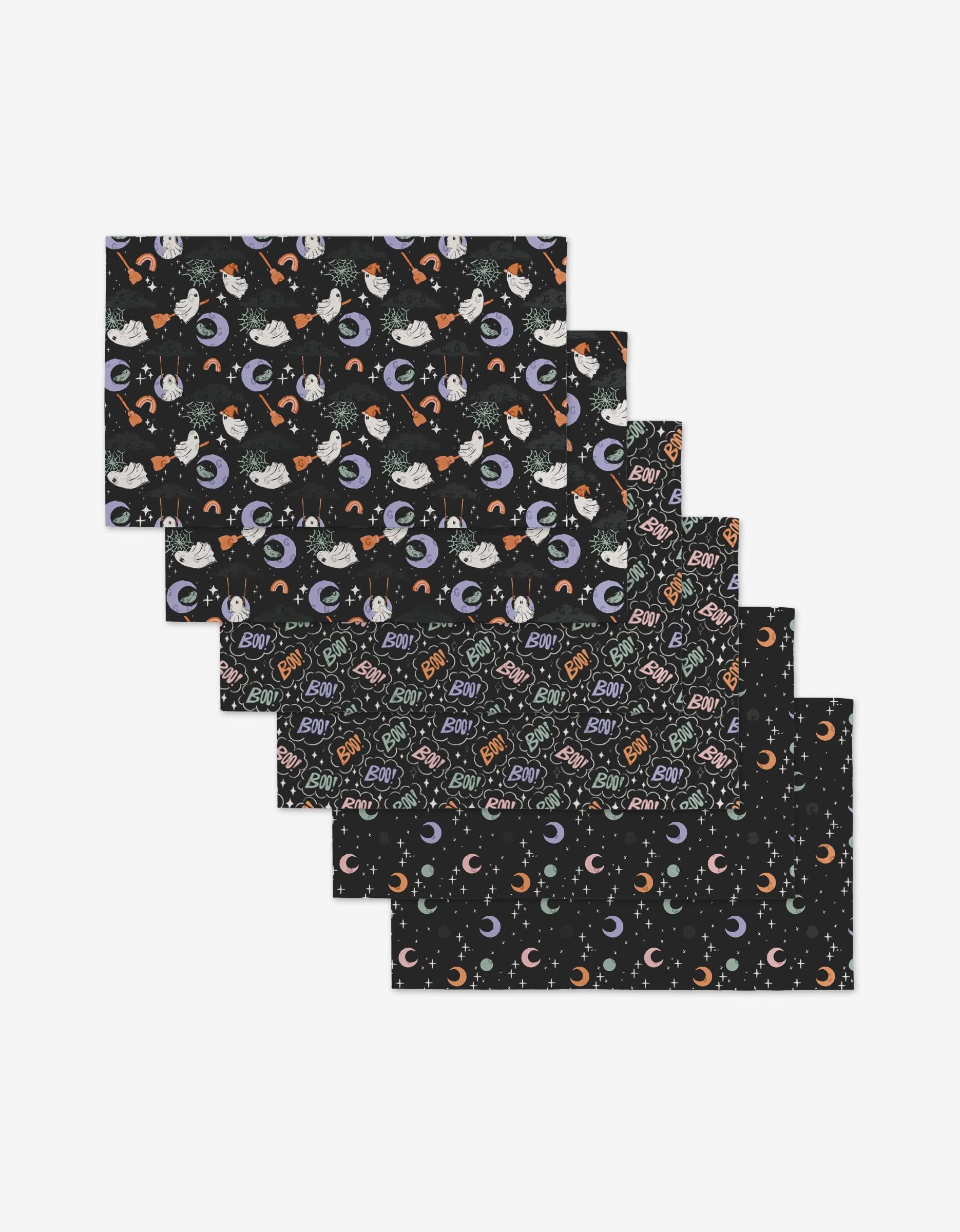 The Ghosts In The Night placemats by Charlie Rowan Designs are a set of six reusable, eco-friendly Halloween-themed mats featuring ghosts, moons, bats, stars, spiderwebs, Boo! text, and candy corn on black backgrounds.