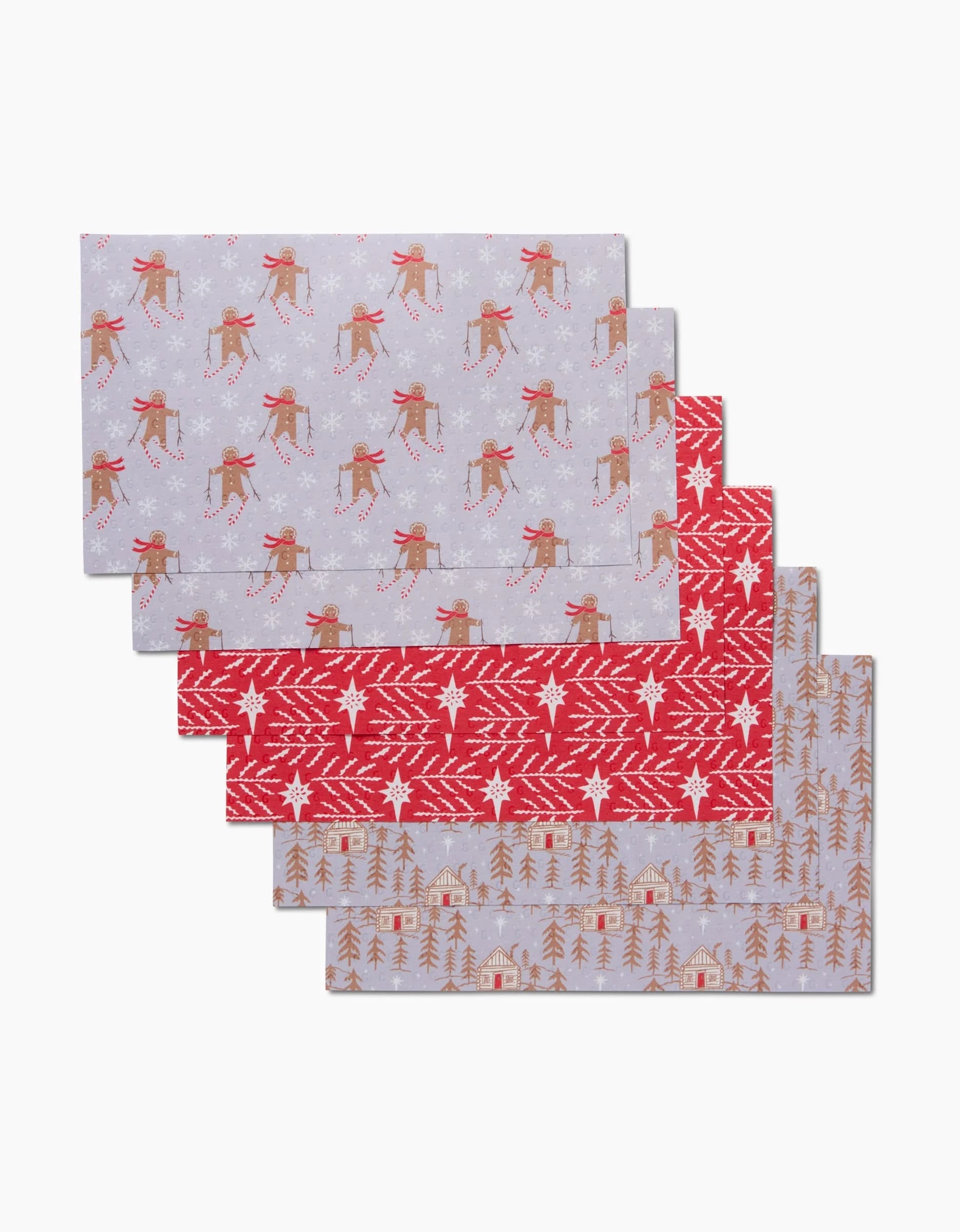 Five “Gingerbread Land” rectangular placemats by Roxy Marj, featuring festive patterns—reindeer on gray, red with white knit design, and cabins among trees on gray—are stacked on a white background.