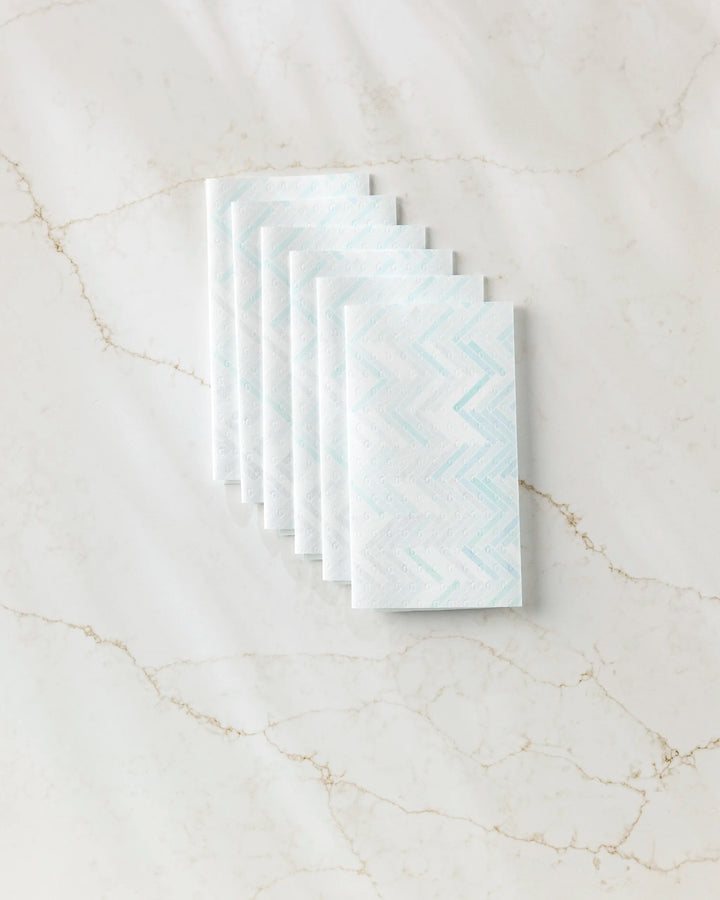 Six folded GEOMETRY "Going Up" reusable paper towels with a blue zigzag pattern are neatly stacked on a white marble surface with subtle brown veins.