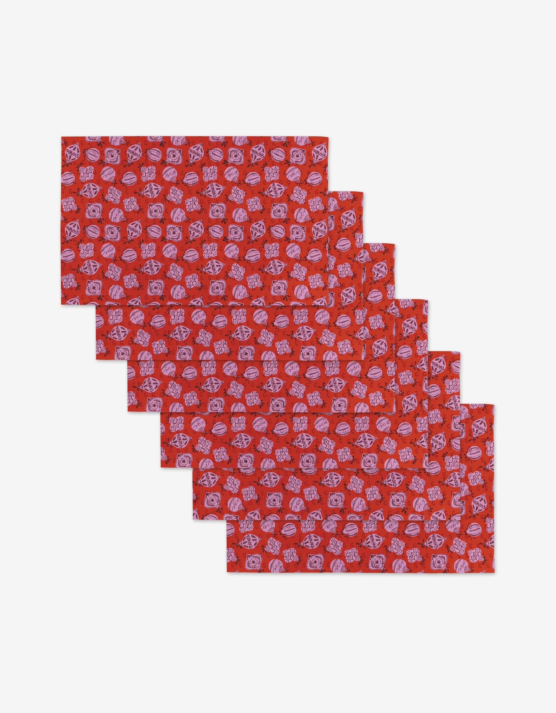 Six Grams Ornaments fabric placemats by Charlie Rowan Designs, featuring a repeating white floral and geometric pattern on red—an eco-friendly alternative to disposable options, shown in a slightly overlapping staggered stack.