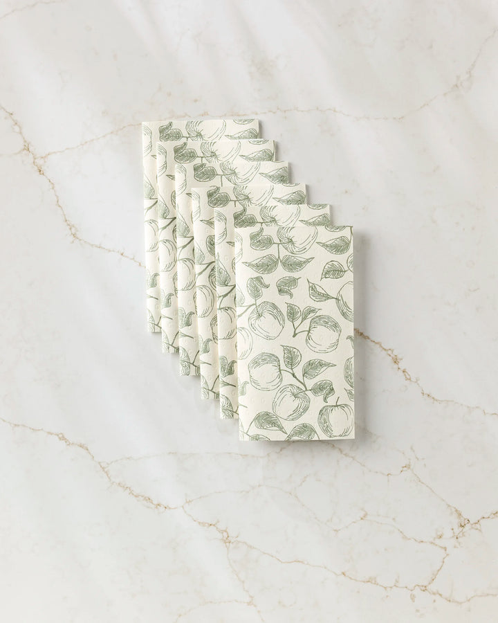 A stack of Ash Cascade Gravenstein Apple reusable paper towels with a green apple and leaf pattern, neatly arranged on a white marble surface with light brown veining.