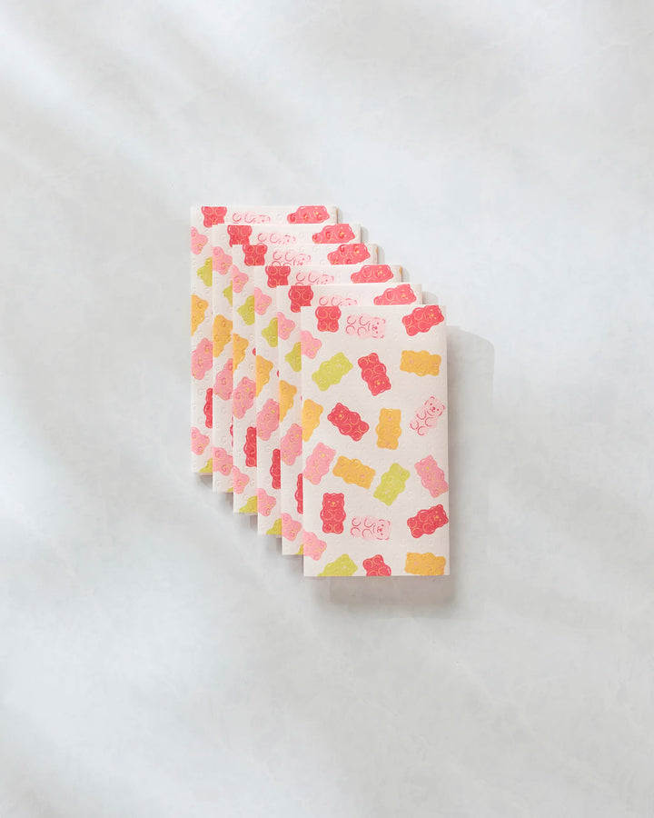 Six "Gummy Bear" chocolate bars by Vaishali Design Studio, wrapped in white paper with colorful gummy bear art, arranged neatly on a marble-like background—evoking playful, eco-friendly kitchen towels.