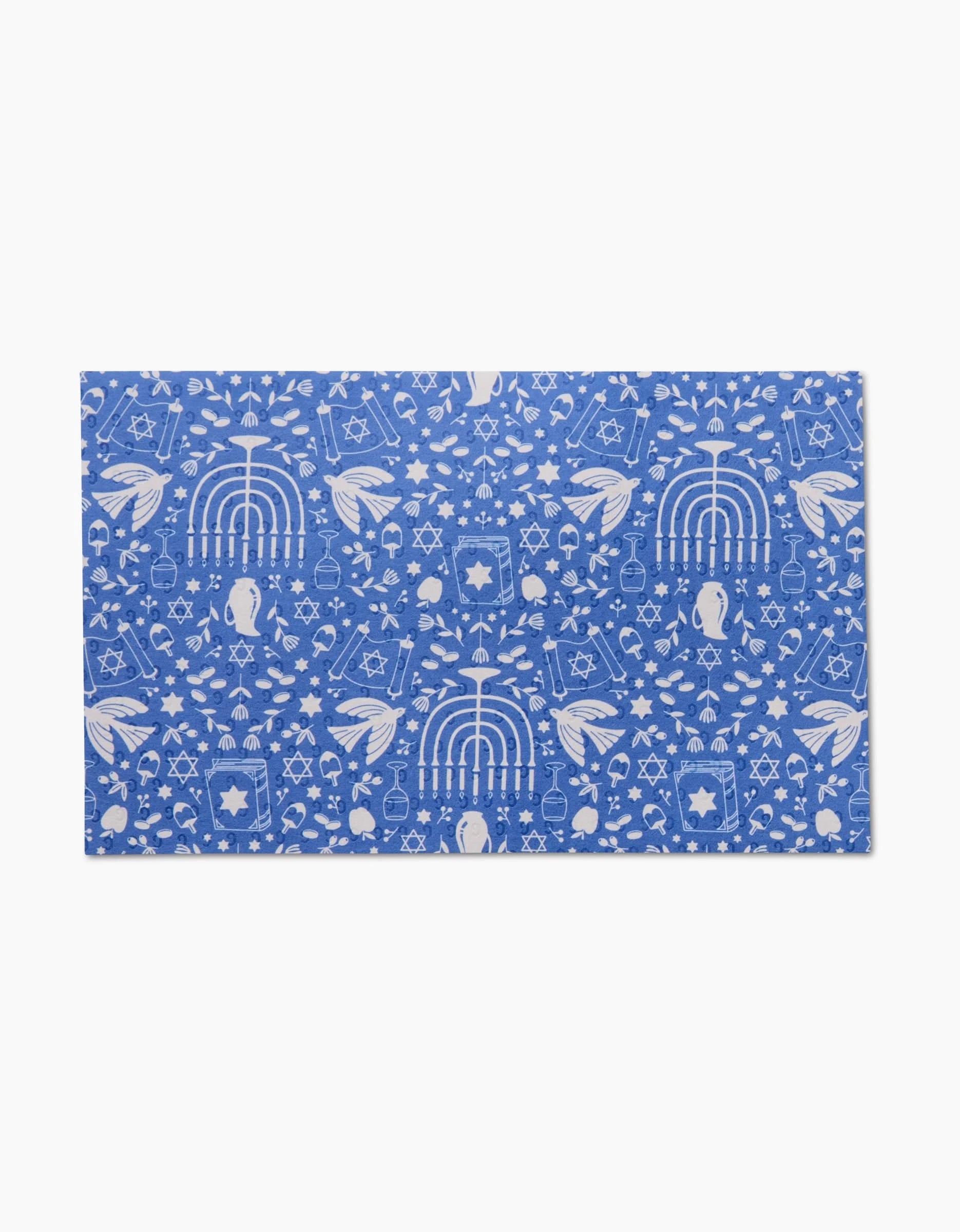 The Hanukkah Sameach by Megan Kampa is a blue rectangular mat with white menorahs and dreidels in a repeating pattern. This eco-friendly, machine-washable mat is ideal as reusable paper towels for the holiday season.