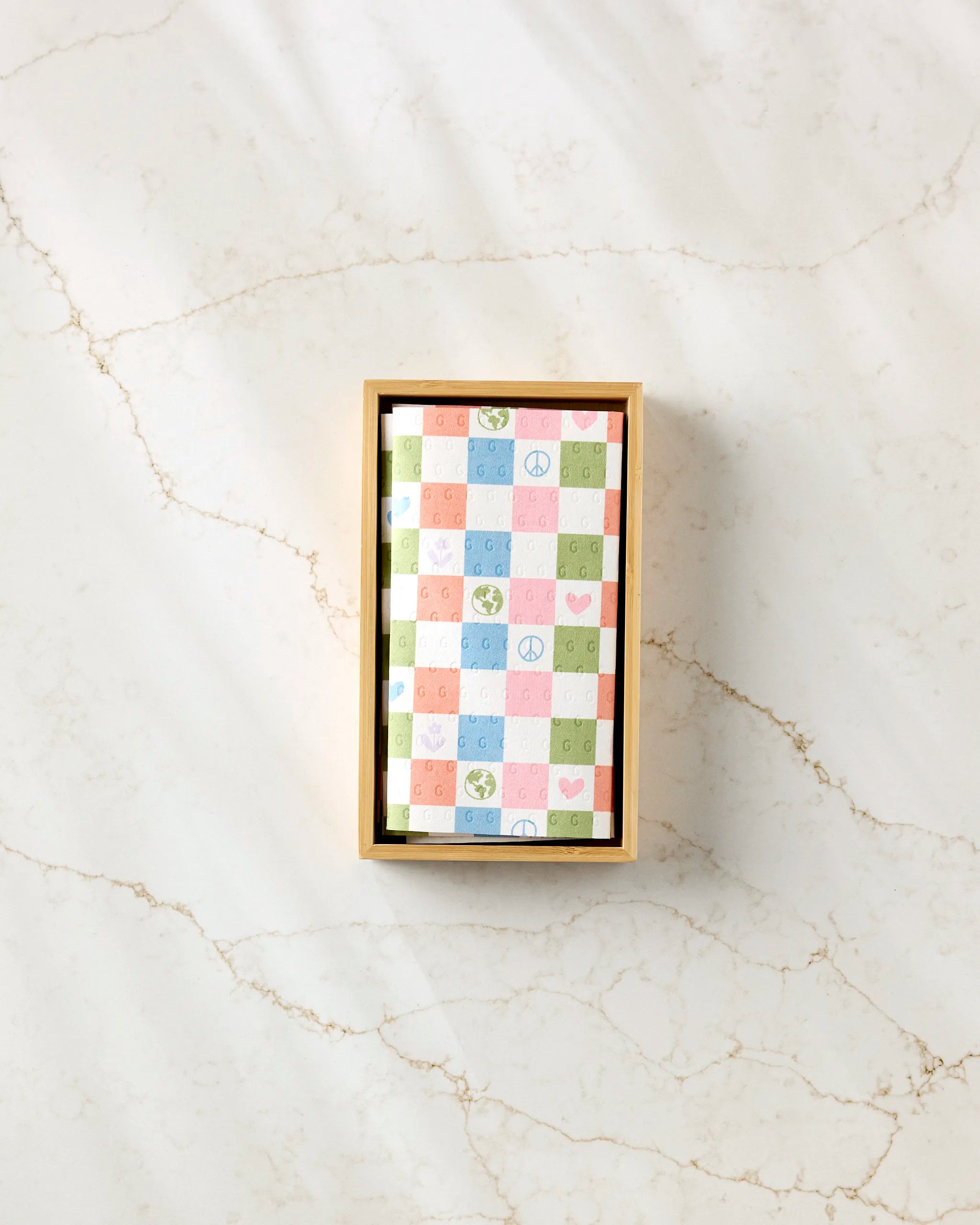 The Kayla Ann Happy Checkers set features reusable paper towels in a rectangular box with pastel checkerboard patterns—green, pink, blue, and orange—adorned with peace signs, hearts, smiley faces, and Earth symbols.