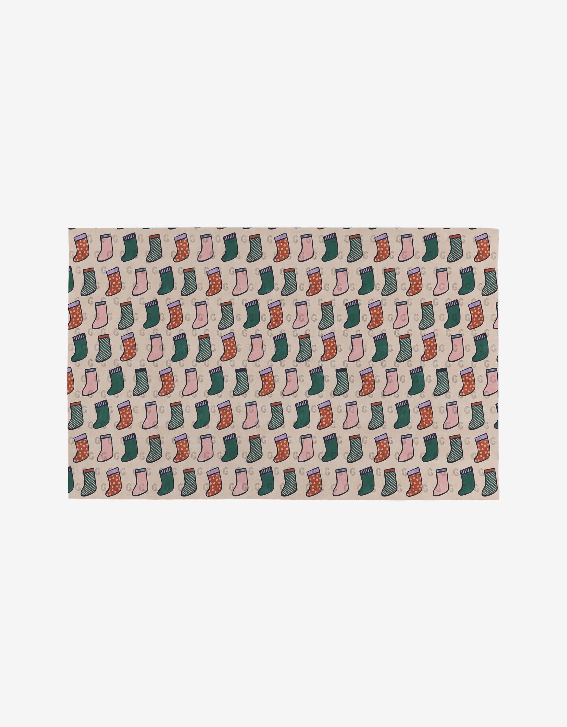 The Happy Holly rectangular mat by Claire Iglesias is made from post-consumer recycled materials and features a cheerful red, green, and pink Christmas stocking pattern on a light beige background.
