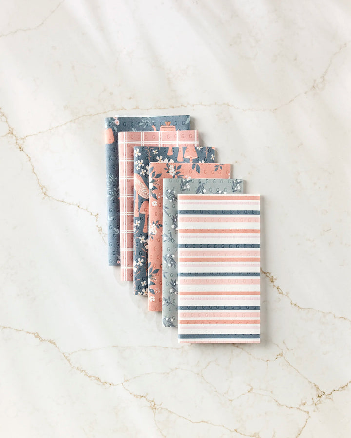 The "Harvest Season" notebook set by Charlie Rowan Designs features six eco-friendly notebooks with floral, animal, and striped pastel covers, fanned out on white marble.