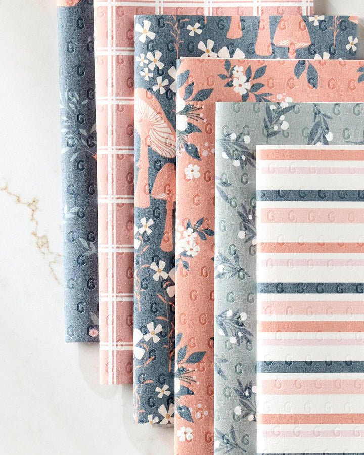 Five patterned eco-friendly "Harvest Season" paper towels by Charlie Rowan Designs, featuring floral, striped, grid, and abstract designs in blue, pink, and white tones, displayed side by side on a white marble surface.