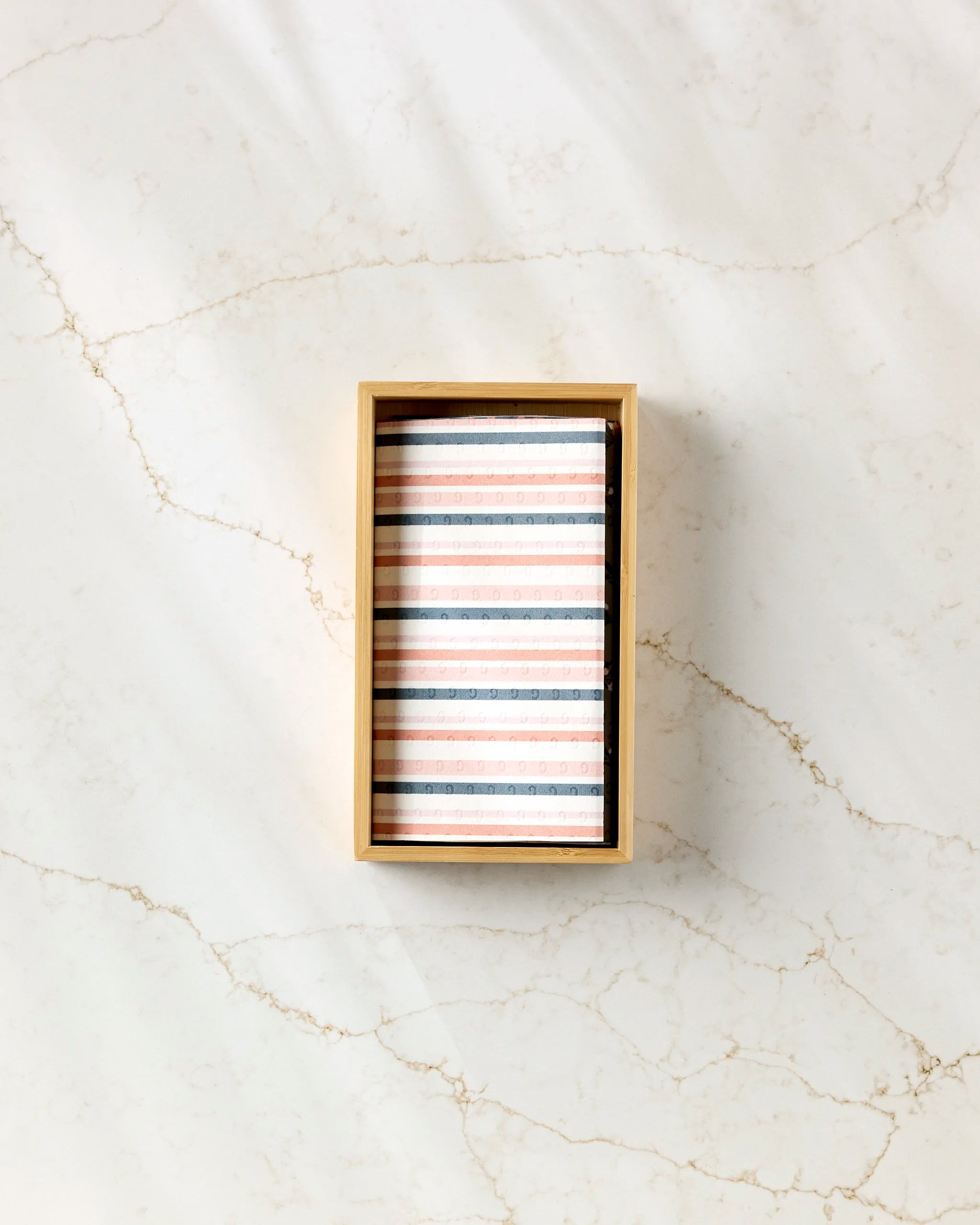 A rectangular box labeled “Harvest Season” by Charlie Rowan Designs showcases neatly stacked, pastel-striped eco-friendly paper towels on a light marble surface with subtle gold veining.