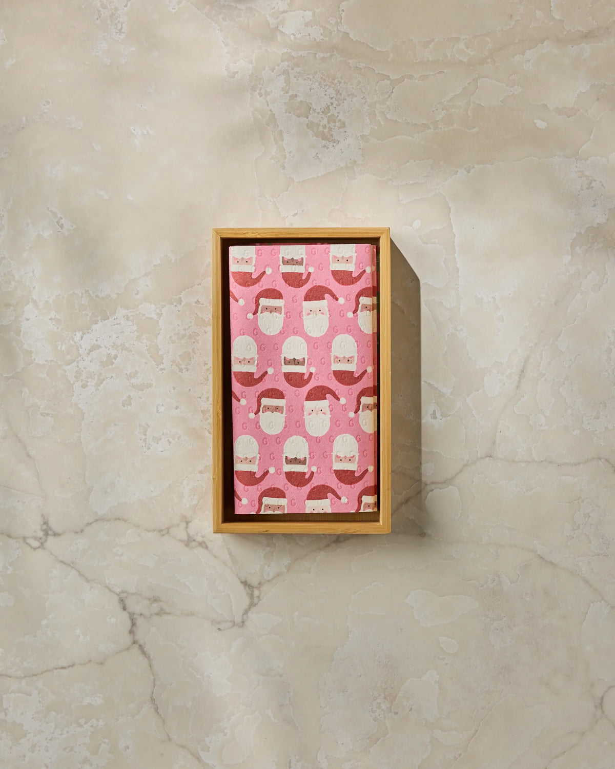 A wooden box with pink wrapping paper decorated with white bears and red scarves sits on a light marble surface, perfect for gifting Geometry’s eco-friendly Holly Jolly Santa kitchen towels or reusable paper towels.