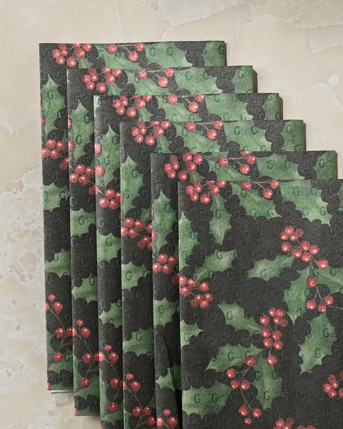 Six reusable “Holly Night” paper towels by Geometry, featuring a festive holly and red berry Christmas design, are fanned out on a light-colored, marble-like surface—an eco-friendly alternative to disposable paper towels that brings seasonal charm to your kitchen.