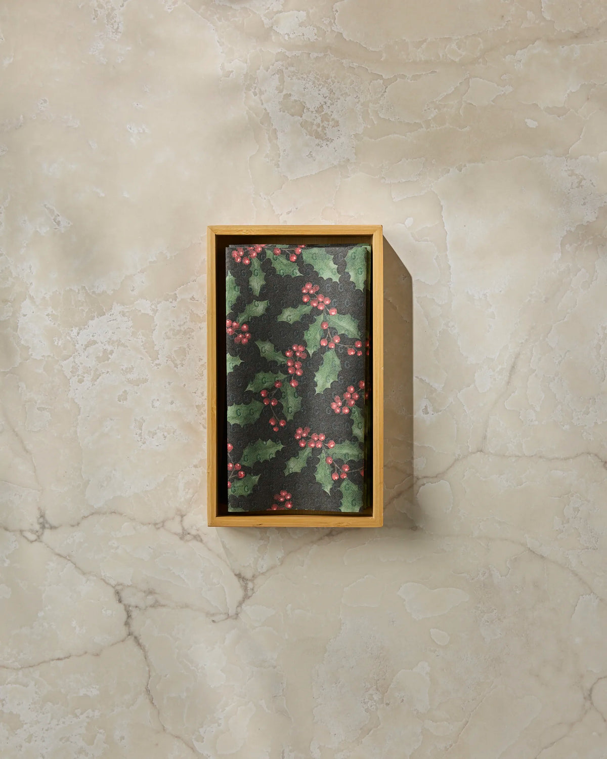 The Geometry Holly Night is a rectangular wooden box with a lid adorned with a holly pattern of green leaves and red berries, displayed on a light marble surface—ideal for storing reusable paper towels as an eco-friendly alternative to disposables in your kitchen.