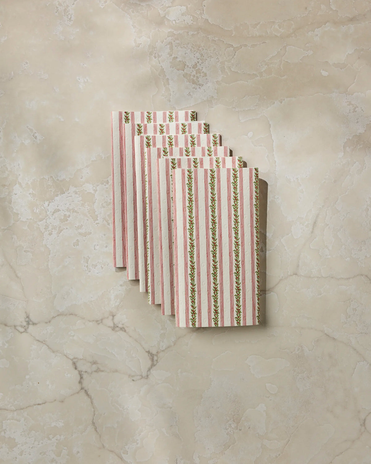 Six Holly Vine reusable paper towels by Geometry—rectangular and striped with a green and pink floral pattern—are neatly fanned out on a beige marble surface.