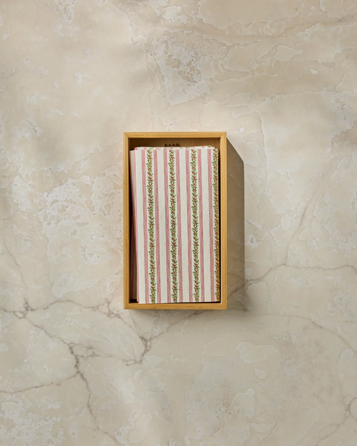 A wooden box on a marble surface holds neatly stacked Holly Vine striped reusable paper towels by Geometry, featuring a floral pattern—an eco-friendly alternative for the modern kitchen.