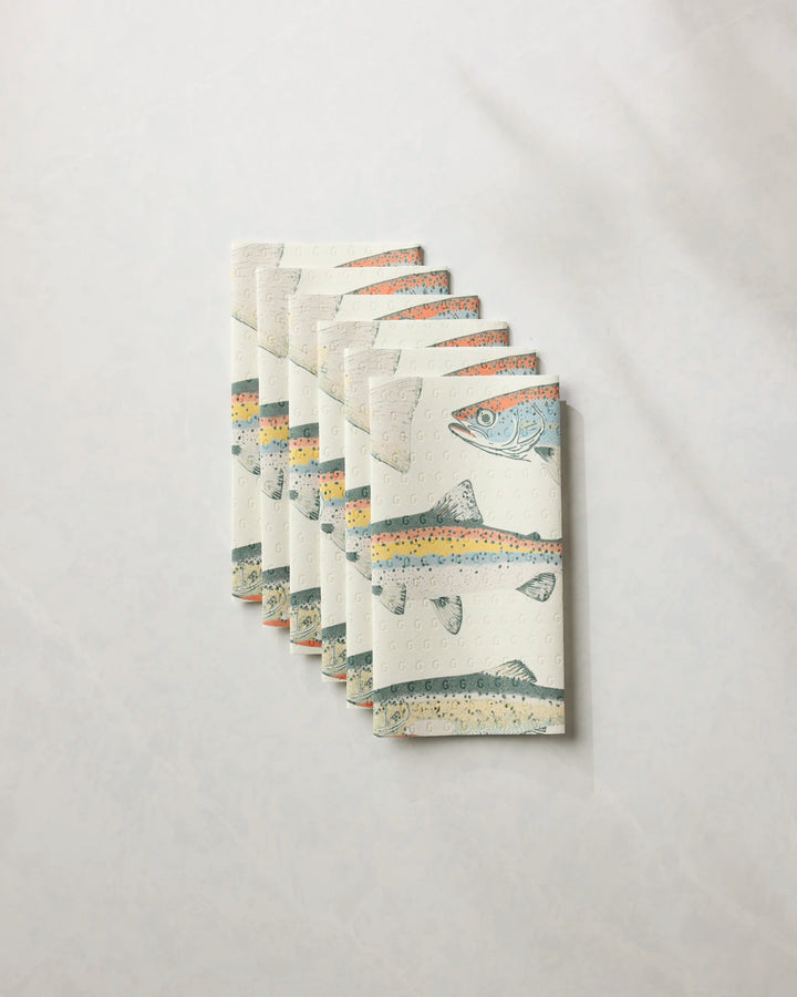 A stack of five folded Geometry kitchen towels from the "Hooked on Fishing" collection, each with a colorful fish design, is displayed on a light, textured background.