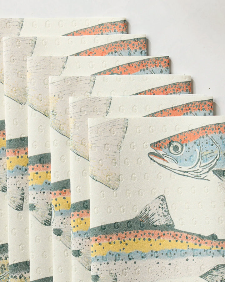 Several "Hooked on Fishing" napkins by Geometry, crafted from eco-friendly kitchen towels, are fanned out. Each features a vibrant fish illustration with detailed orange, yellow, and blue scales.