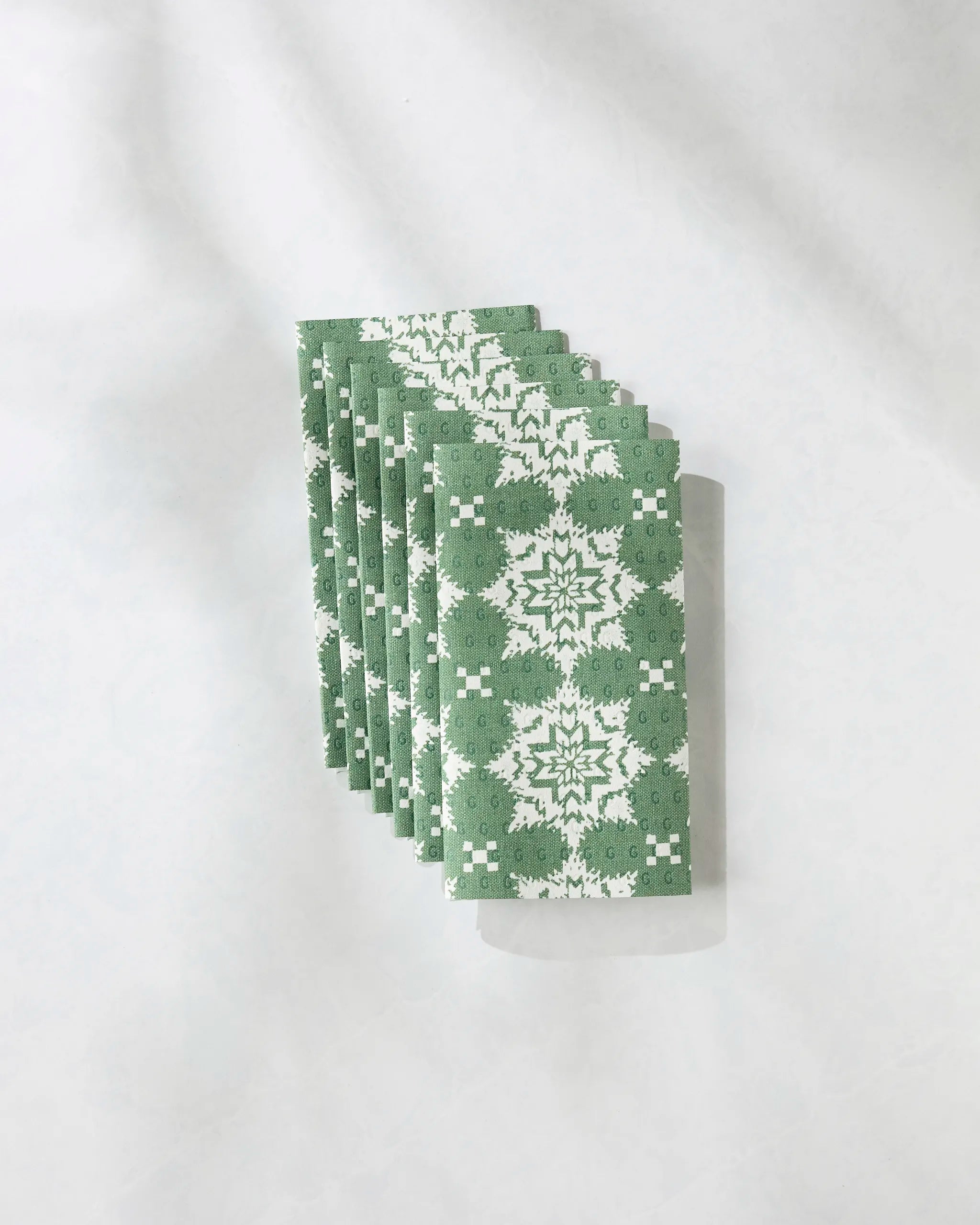 A stack of Geometry’s Iceflower Green reusable paper towels, featuring a symmetrical green and white floral pattern, is neatly arranged on a light surface, with shadows cast to the right.