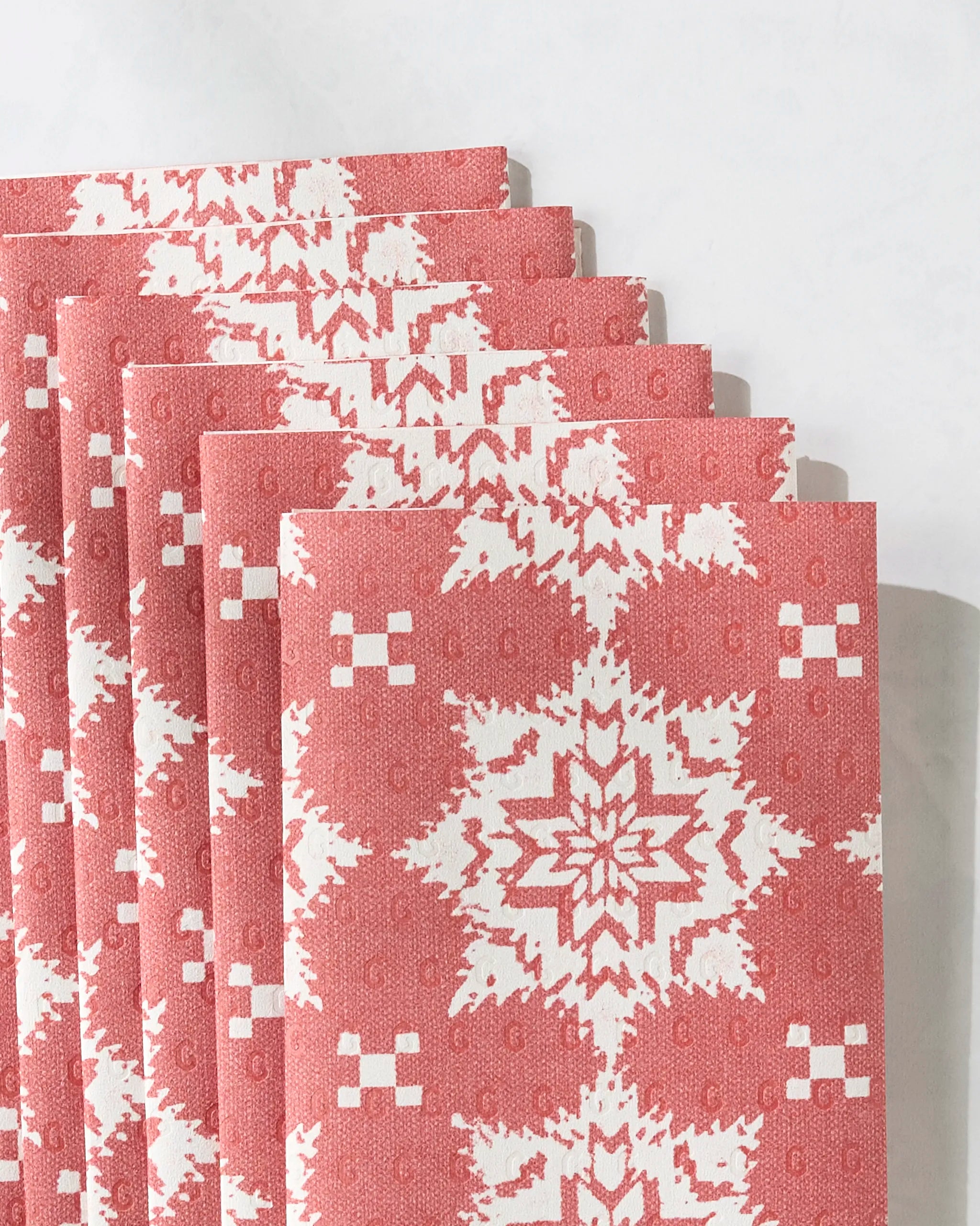 Five folded Iceflower Red reusable paper towels by Geometry, featuring a white snowflake and geometric pattern, are stacked neatly on a light surface.