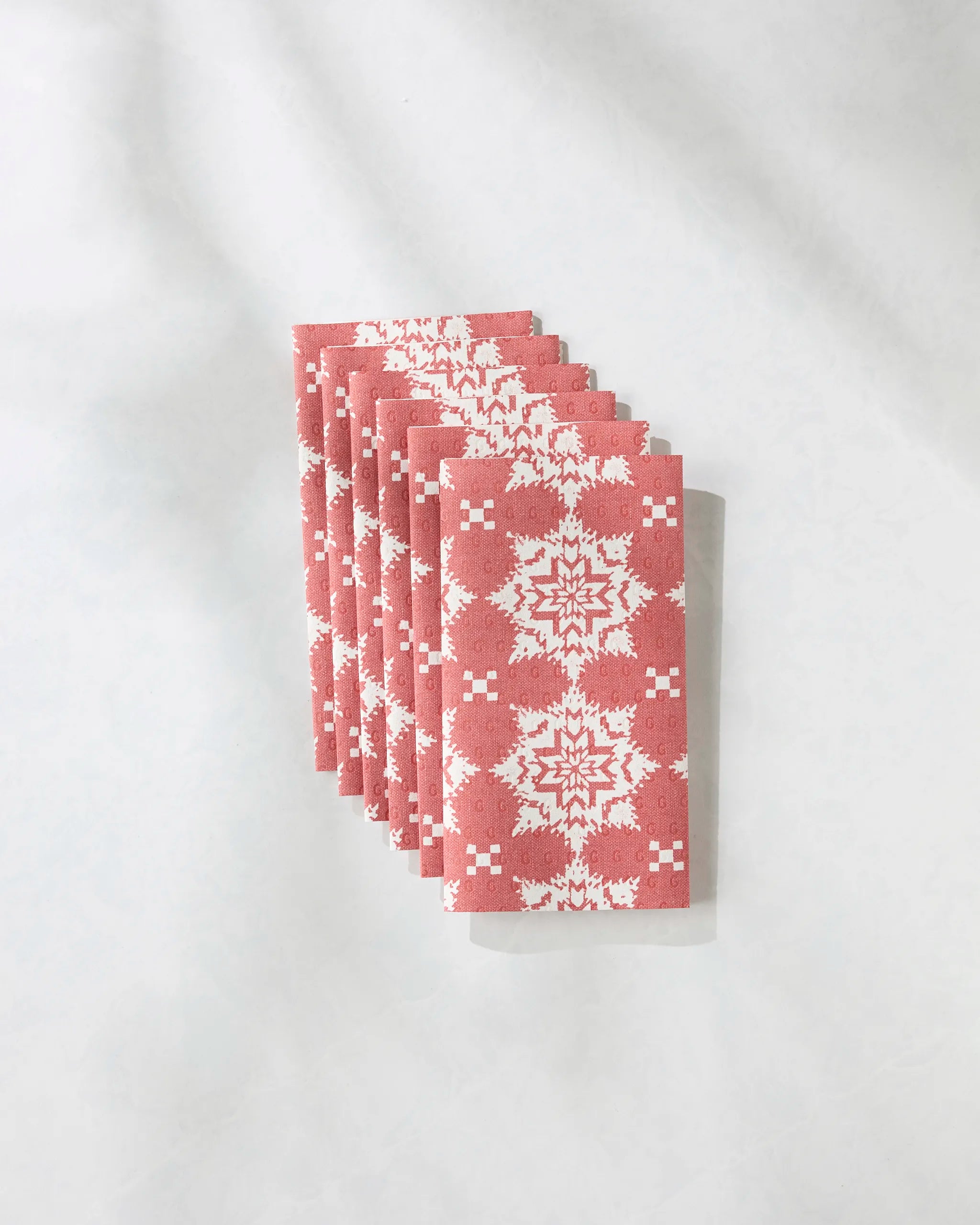 Six folded Iceflower Red napkins by Geometry, featuring a white snowflake pattern and made from eco-friendly paper, are neatly stacked on a light gray surface.