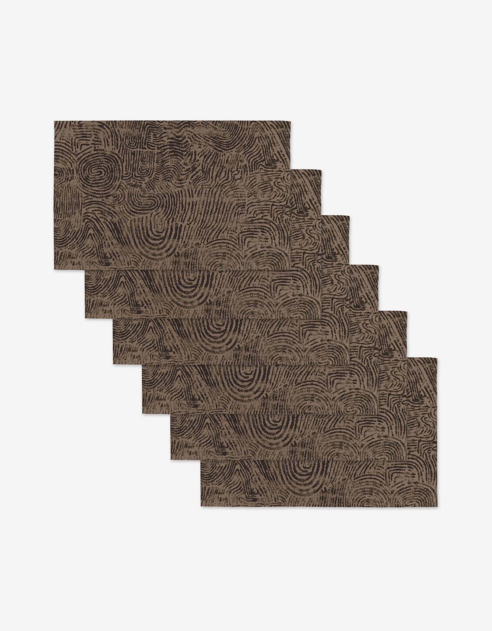Six Imprint rectangular brown placemats by Studio Jeannot, each with a black fingerprint-inspired swirl design, are stacked diagonally on a white background—elegant, reusable, and eco-friendly alternatives to paper towels.